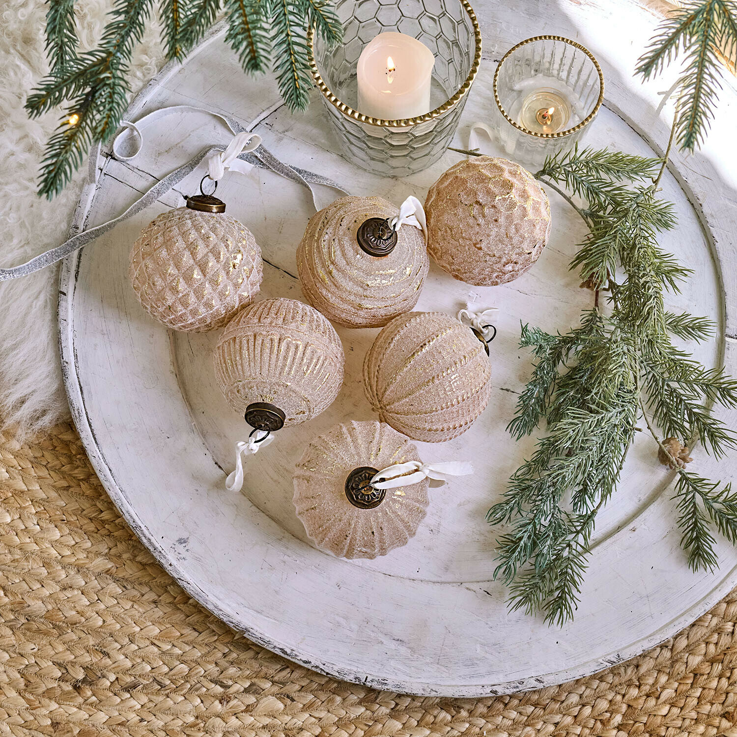 Sechsteiliges Set rosa-goldener Glas-Weihnachtskugeln auf weißem Tablett mit Tannenzweigen dekoriert