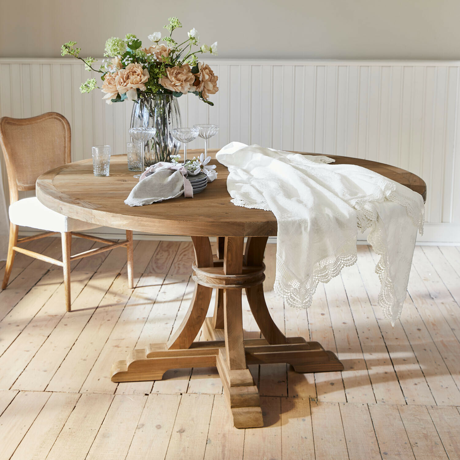 Runder Holztisch mit weißer Spitzen-Tischdecke und Blumenstrauß in Glasvase