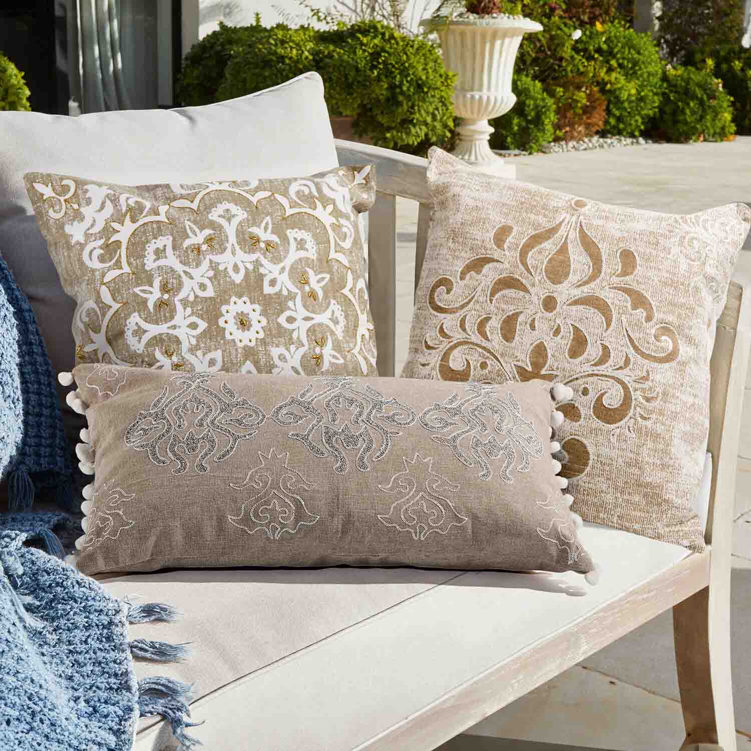 Drei dekorative Kissen in Beige und Weiß mit Mustern auf hellem Sofa im Garten