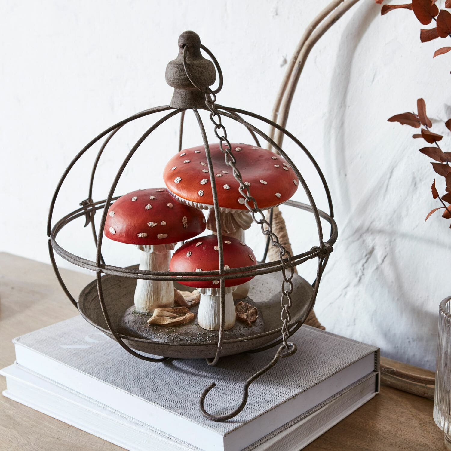 Voliere Valère Dekorative rote Fliegenpilze aus Kunststoff in Metallkäfig auf Büchern auf Holztisch