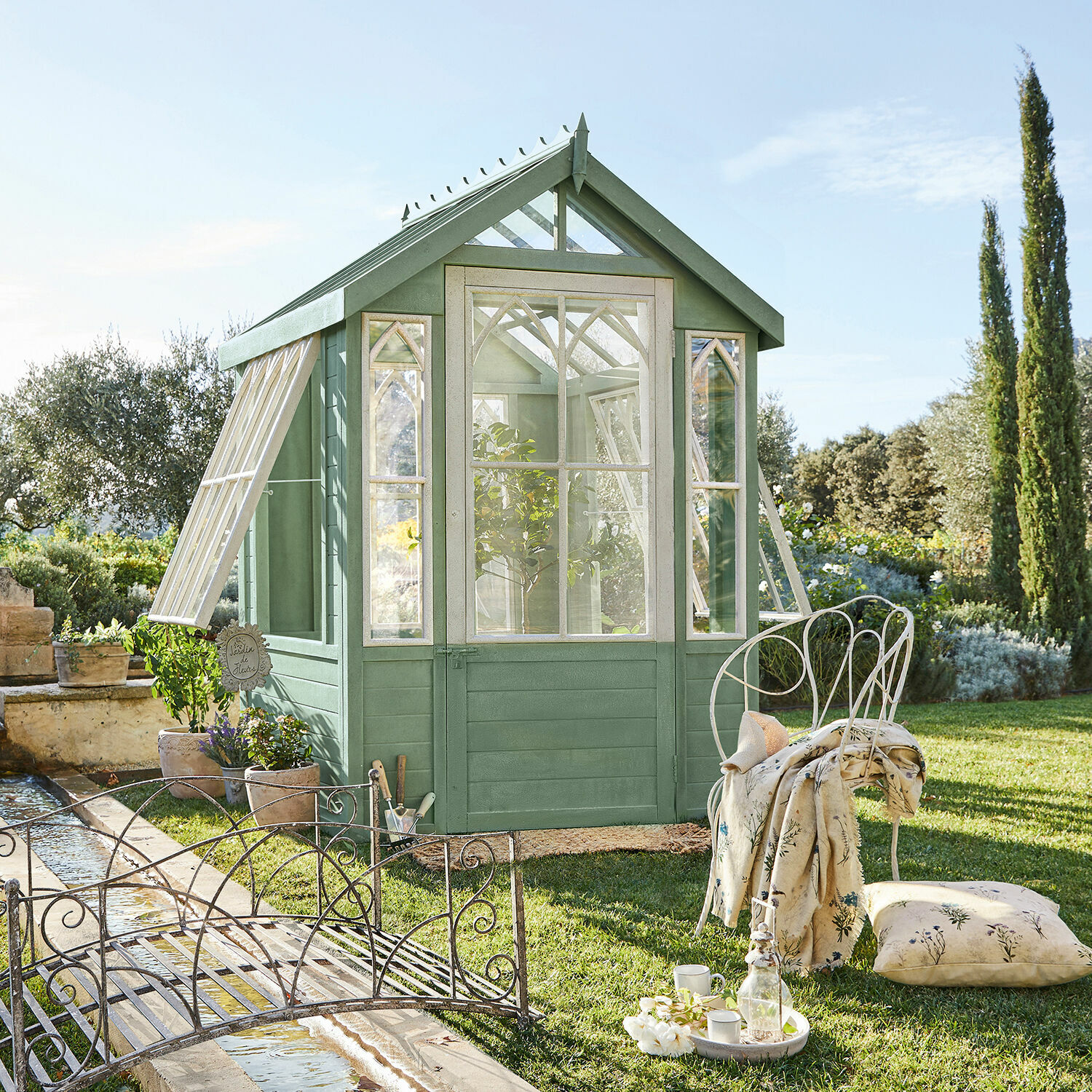 Gartenhaus Anyós Grüne Holz-Gewächshaus mit weißen Fenstern und Metallmöbeln auf dem Rasen im Garten