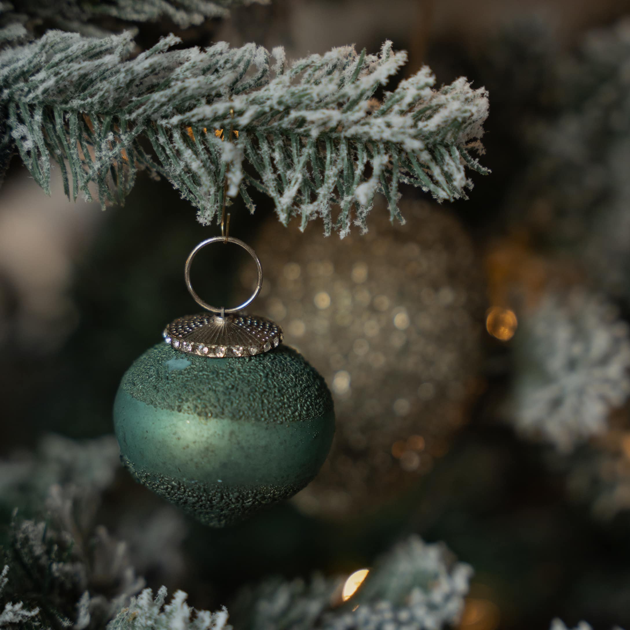 Grüne matte Weihnachtskugel mit strukturierter Oberfläche und silberner Aufhängung an verschneigtem Zweig