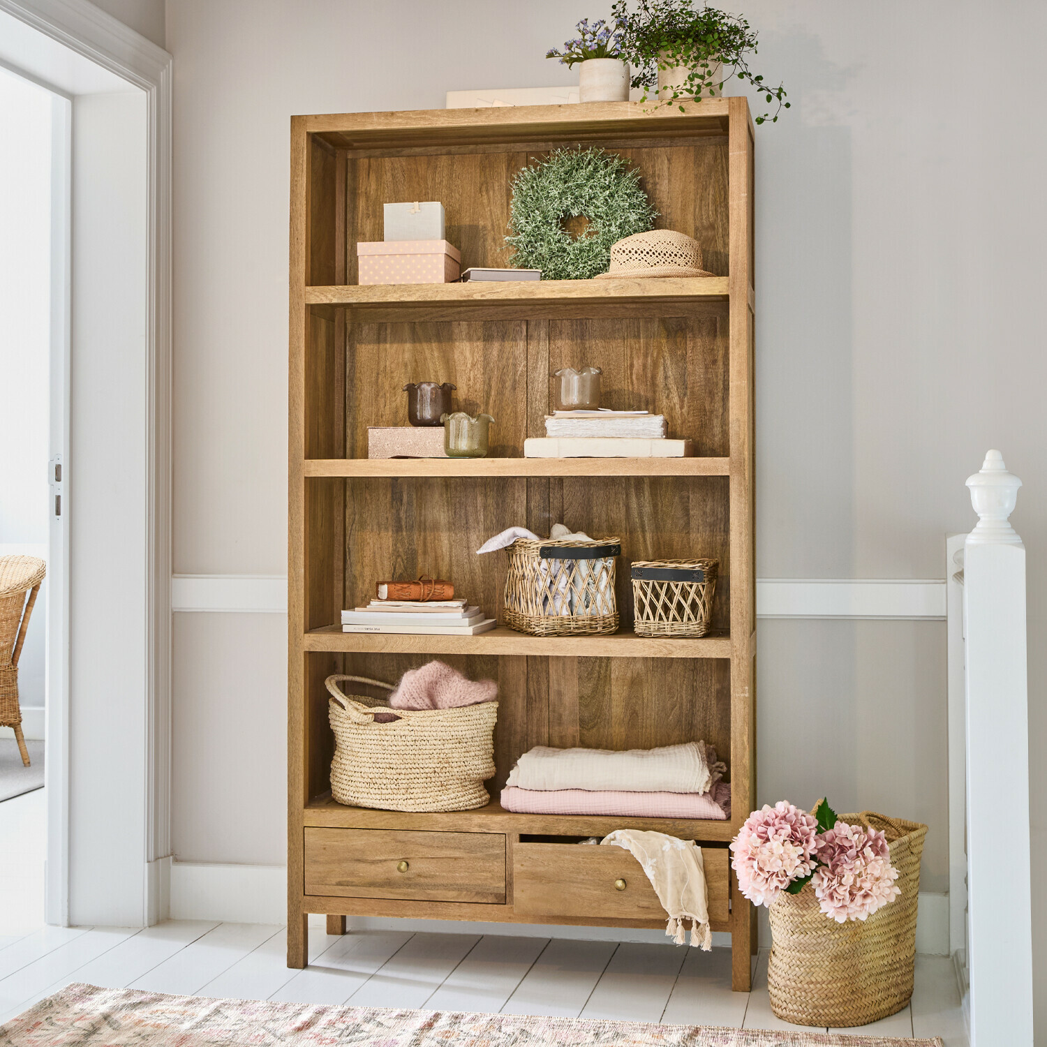 Holzregal mit vier Fächern und zwei Schubladen, dekoriert mit Körben und hellen Textilien
