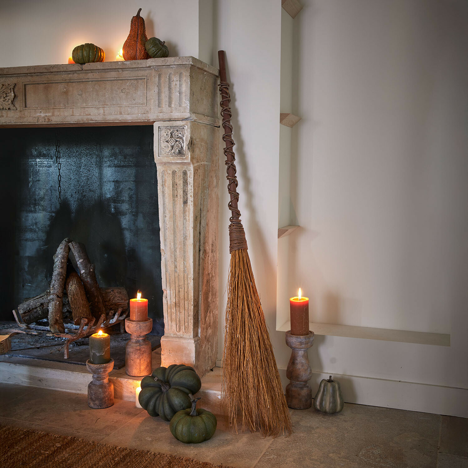 Deko-Besen Maerlinna Natürlicher Reisigbesen an einem Steinkamin mit grünen Kürbissen und brennenden Kerzen im rustikalen Raum