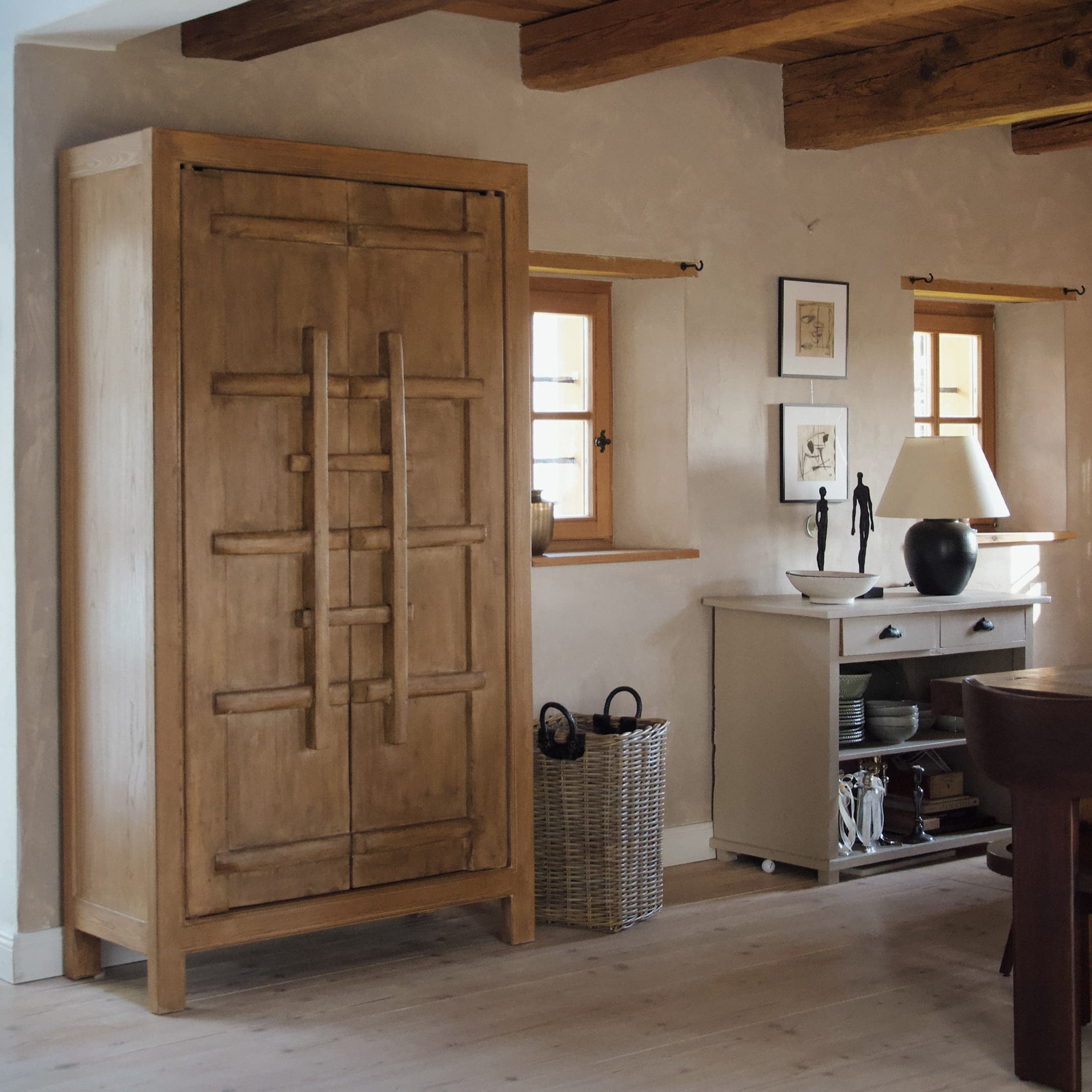 Holzschrank in Naturfarbe in rustikalem Raum mit Korb aus Weide und weißem Sideboard