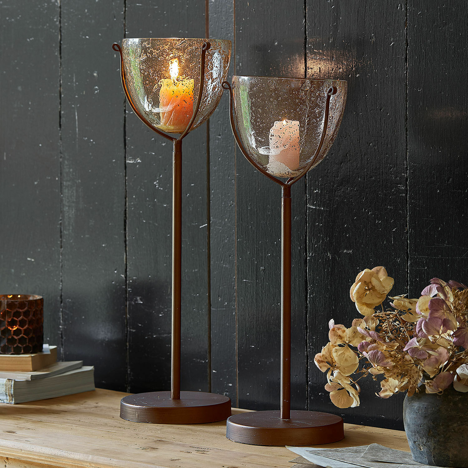 Kerzenständer 2er Set Piacello Zwei braune Metall-Kerzenhalter mit geblasenem Glas und brennenden Kerzen auf Holztisch