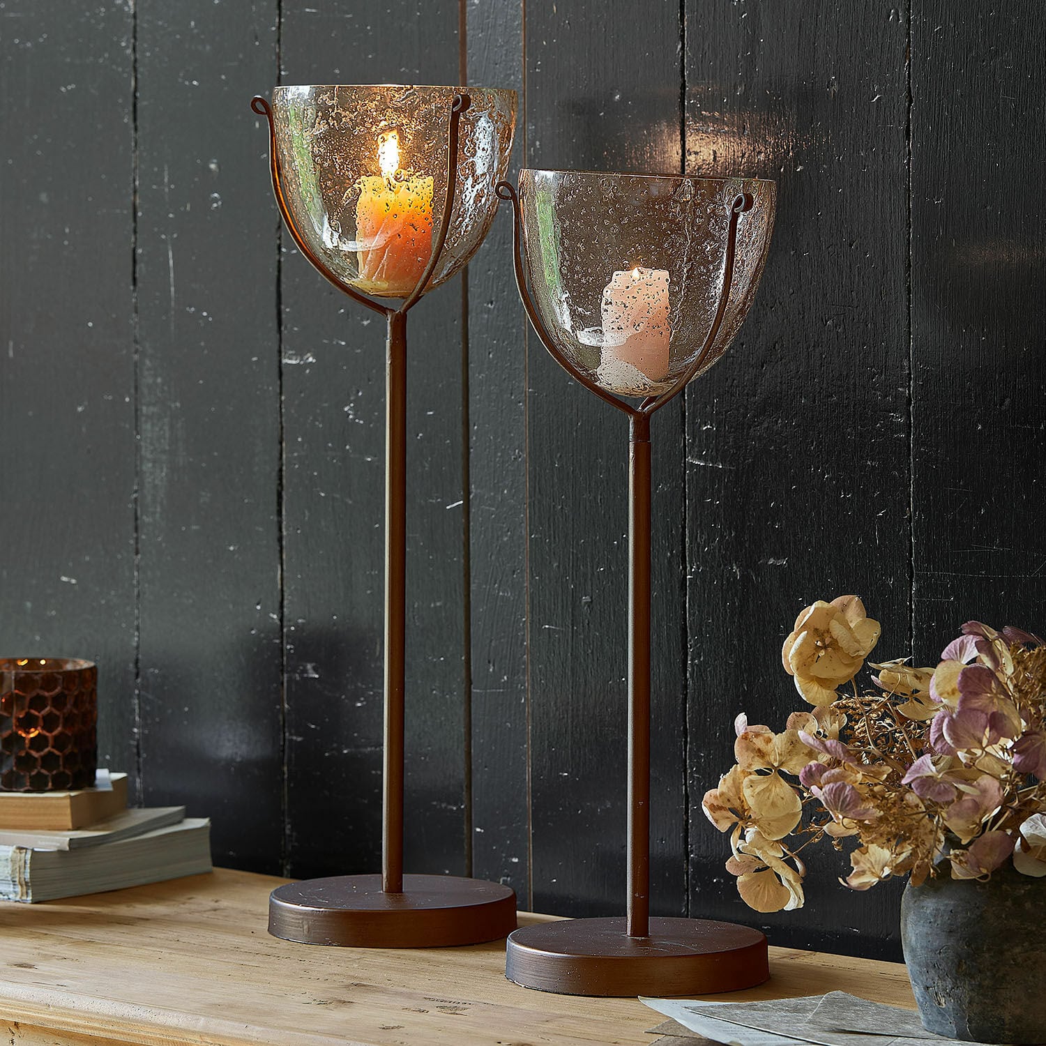 Kerzenständer 2er Set Piacello Zwei braune Metall-Kerzenhalter mit geblasenem Glas und brennenden Kerzen auf Holztisch