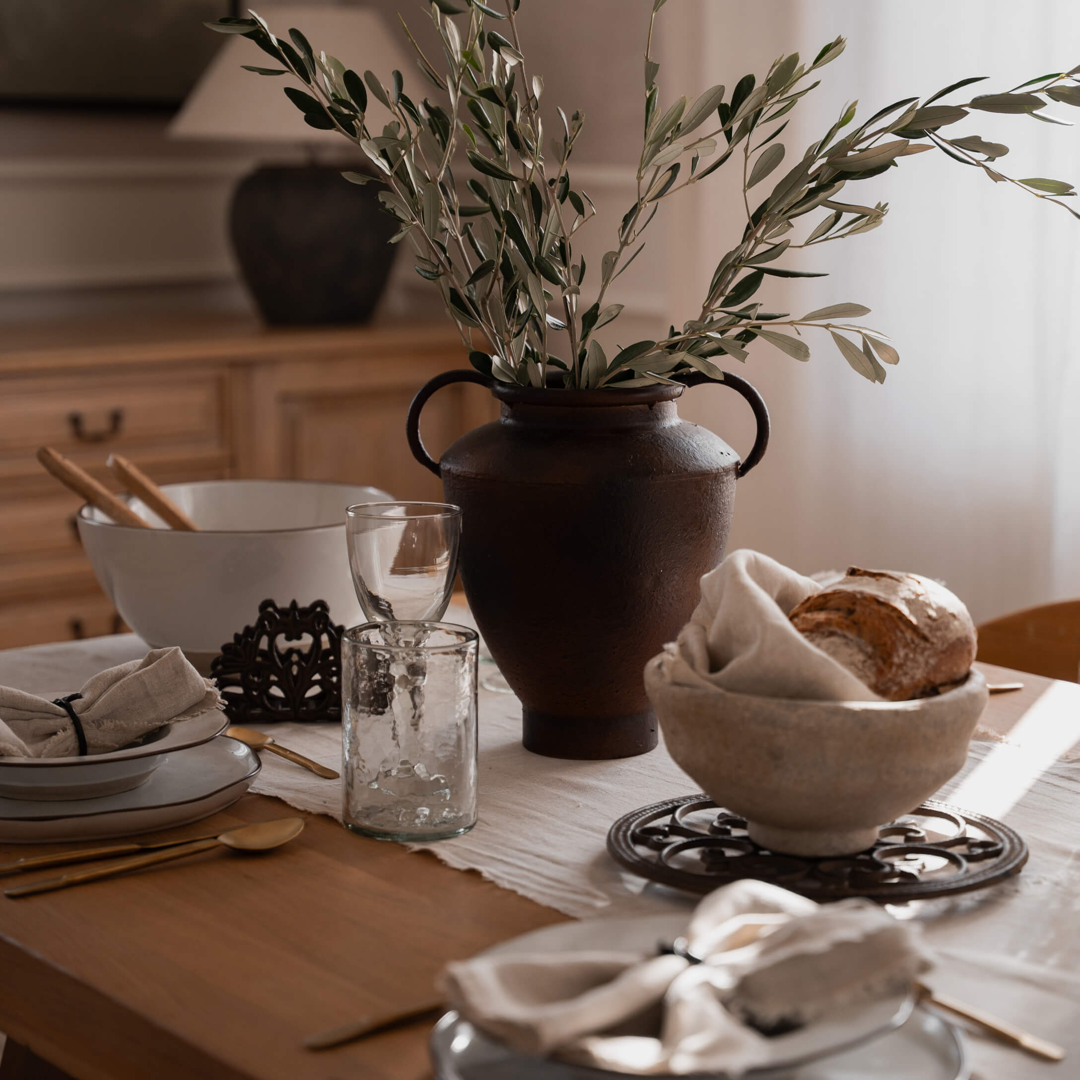 Rustikaler brauner Keramikvase mit grünen Zweigen auf Holztisch mit Geschirr
