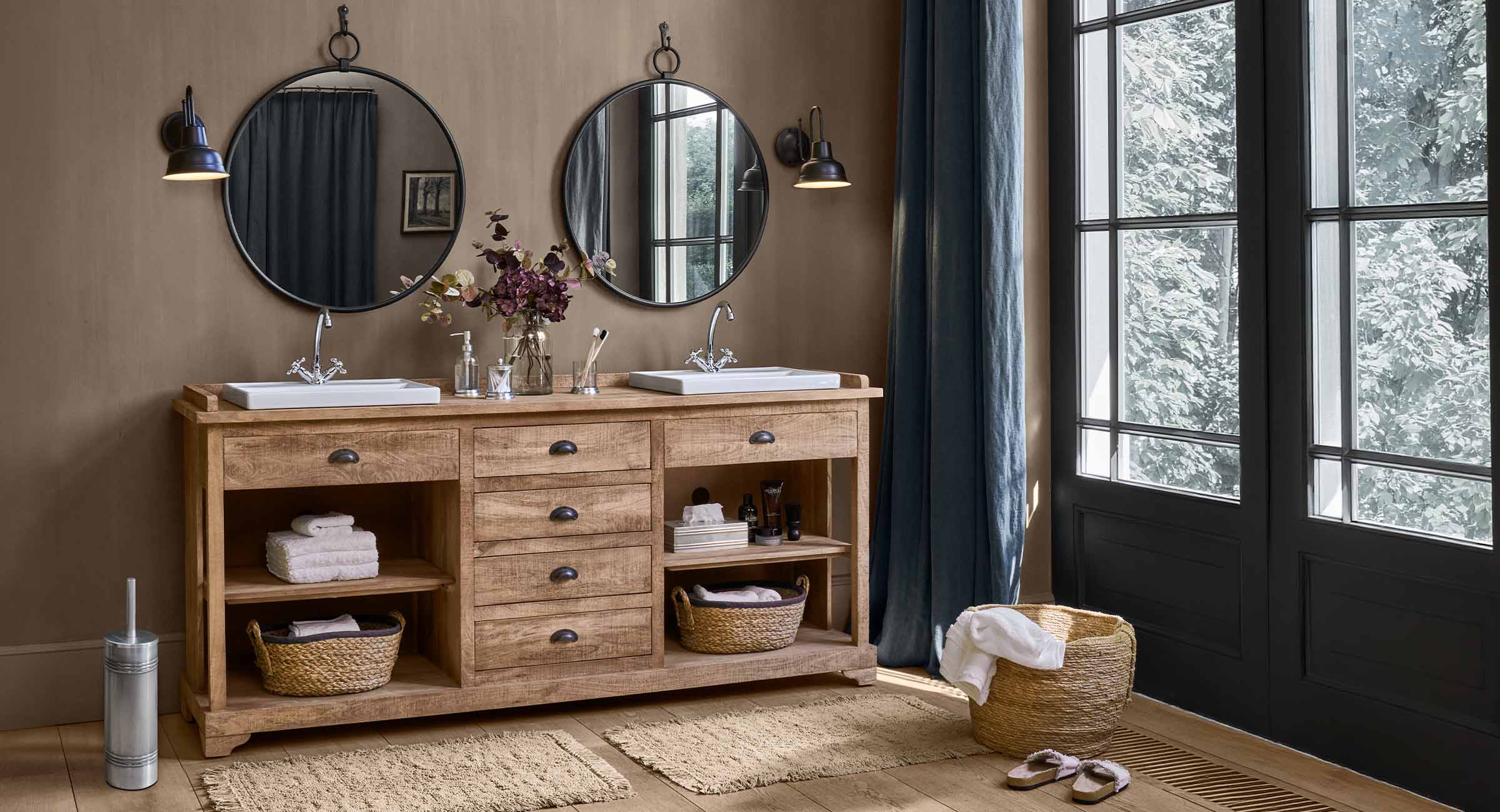 Holz-Badezimmerschrank mit zwei weißen Waschbecken und runden Spiegeln in natürlichem Ambiente
