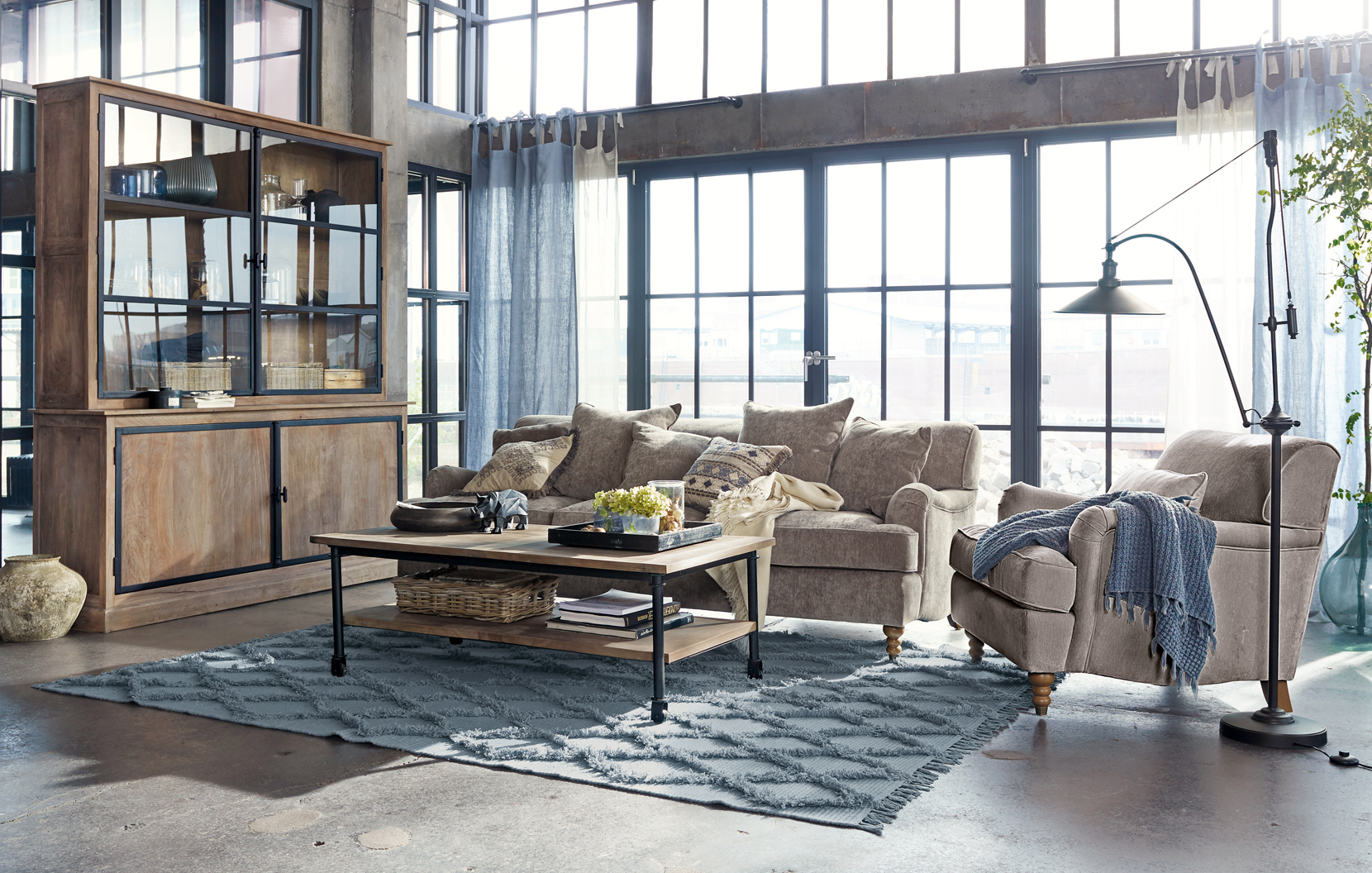 Gemütliches Loft-Wohnzimmer mit beigem Sofa, Holzvitrine und blauem Teppich auf Betonboden