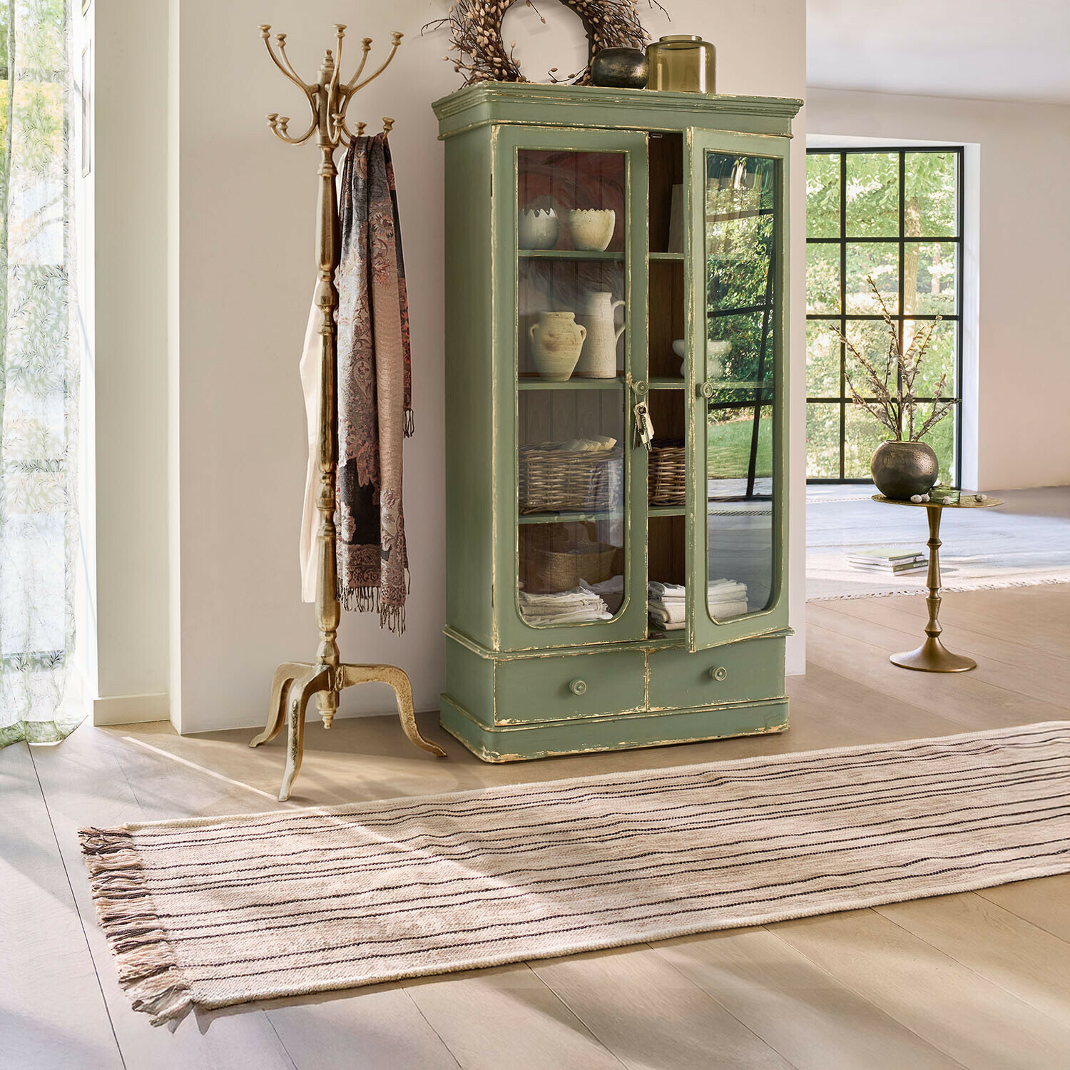 Grüner Holzvitrinenschrank mit Glastüren und Schublade im hellen Vintage-Wohnzimmer