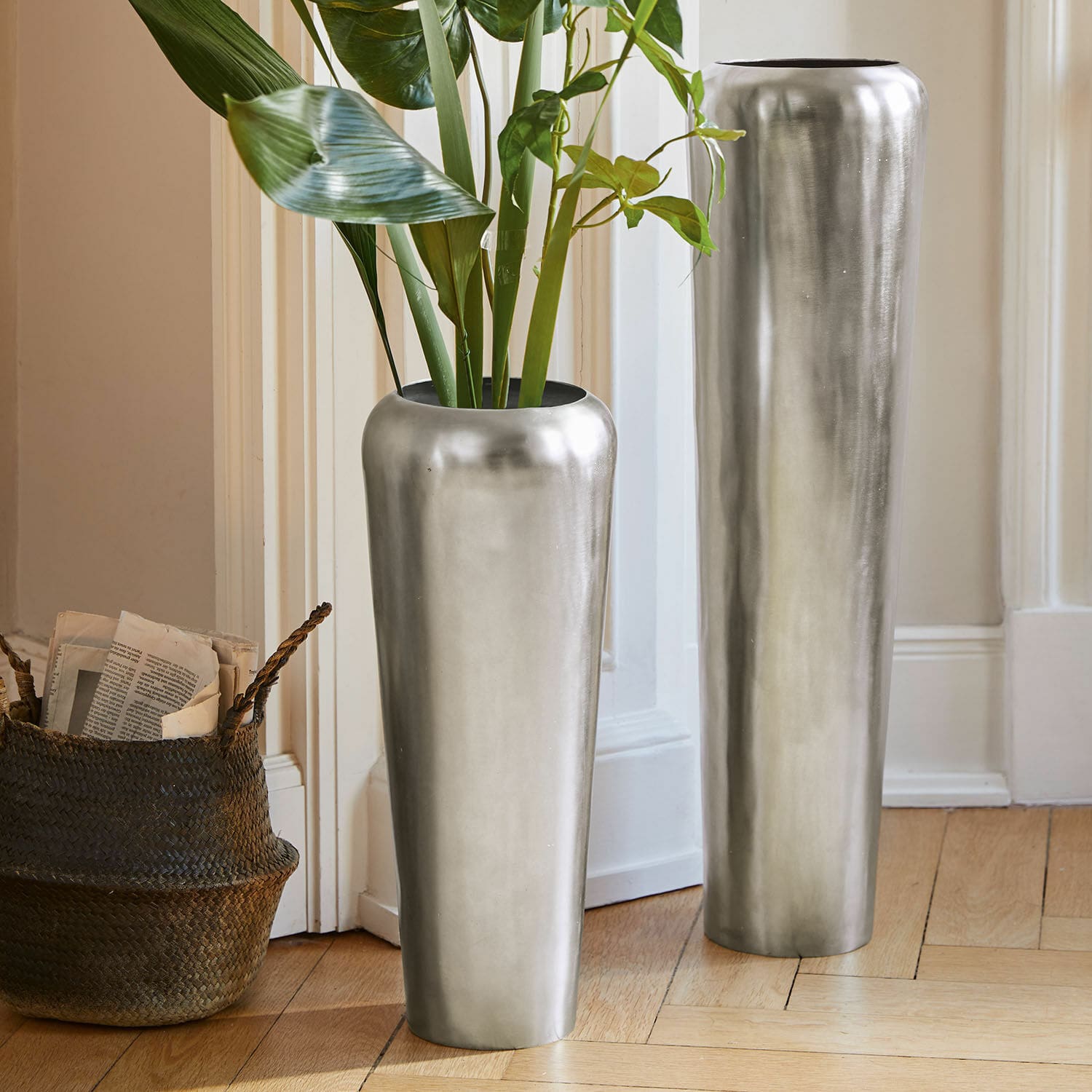Bodenvase 2er Set Carolan Zwei hohe silberne Metallvasen auf dem Boden in hellem Raum mit grünen Pflanzen