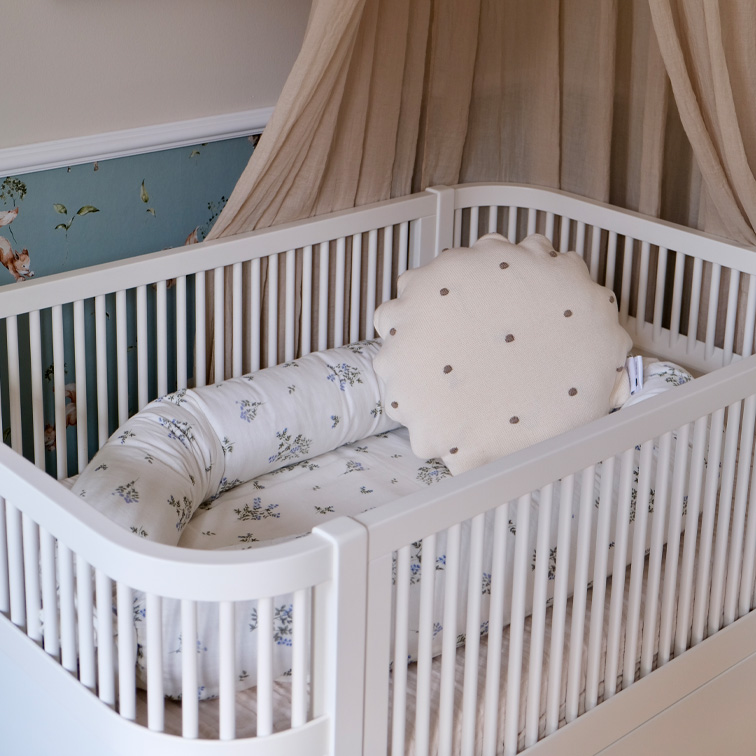 Weißes Babybett mit weichem Kissen und floral gemustertem Bettzeug in Pastellfarben