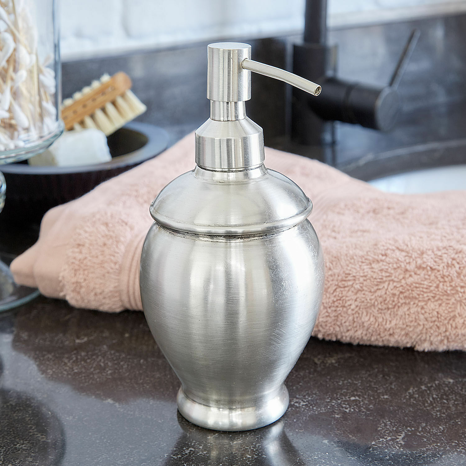 Silberner Metall-Seifenspender auf Waschtisch mit rosa Handtuch im Hintergrund