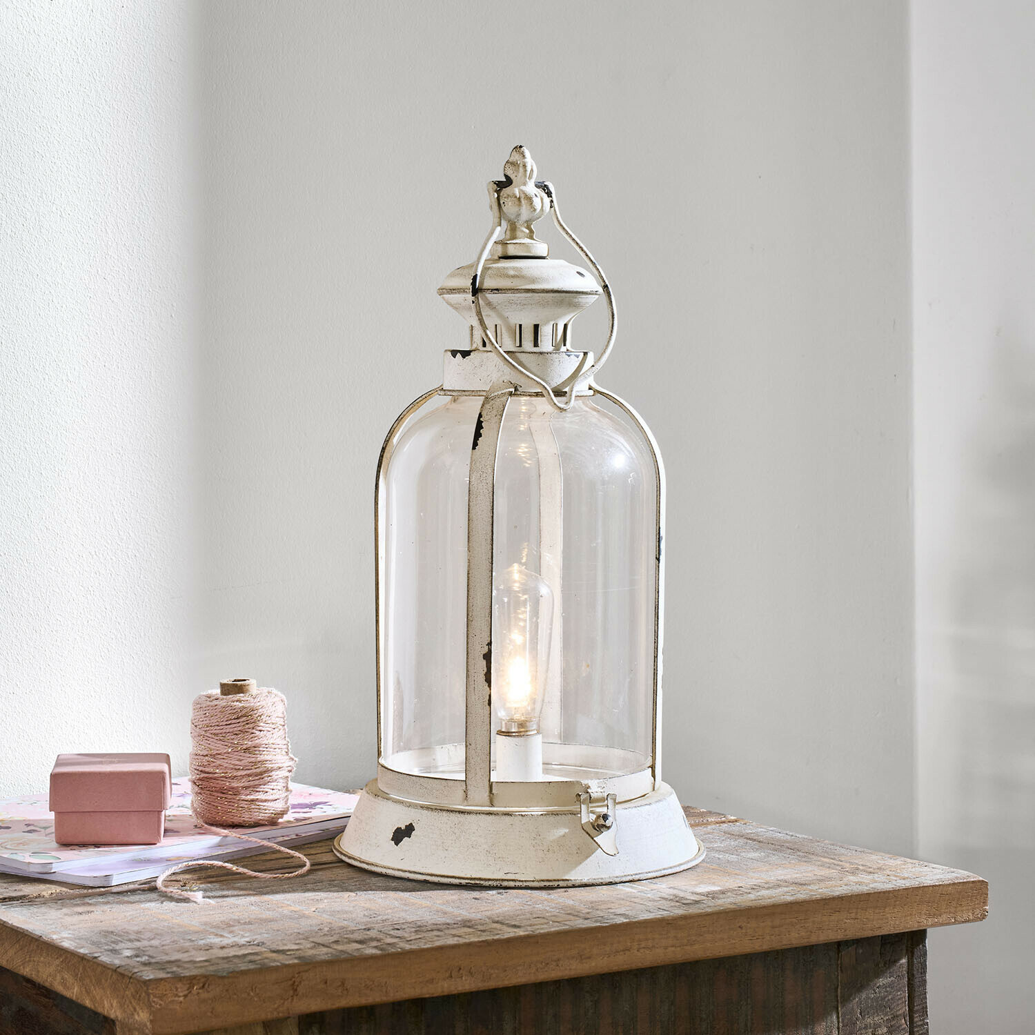 Weiße Metalllaterne mit klarem Glas und Glühbirne auf Holztisch, dekorative Innenbeleuchtung