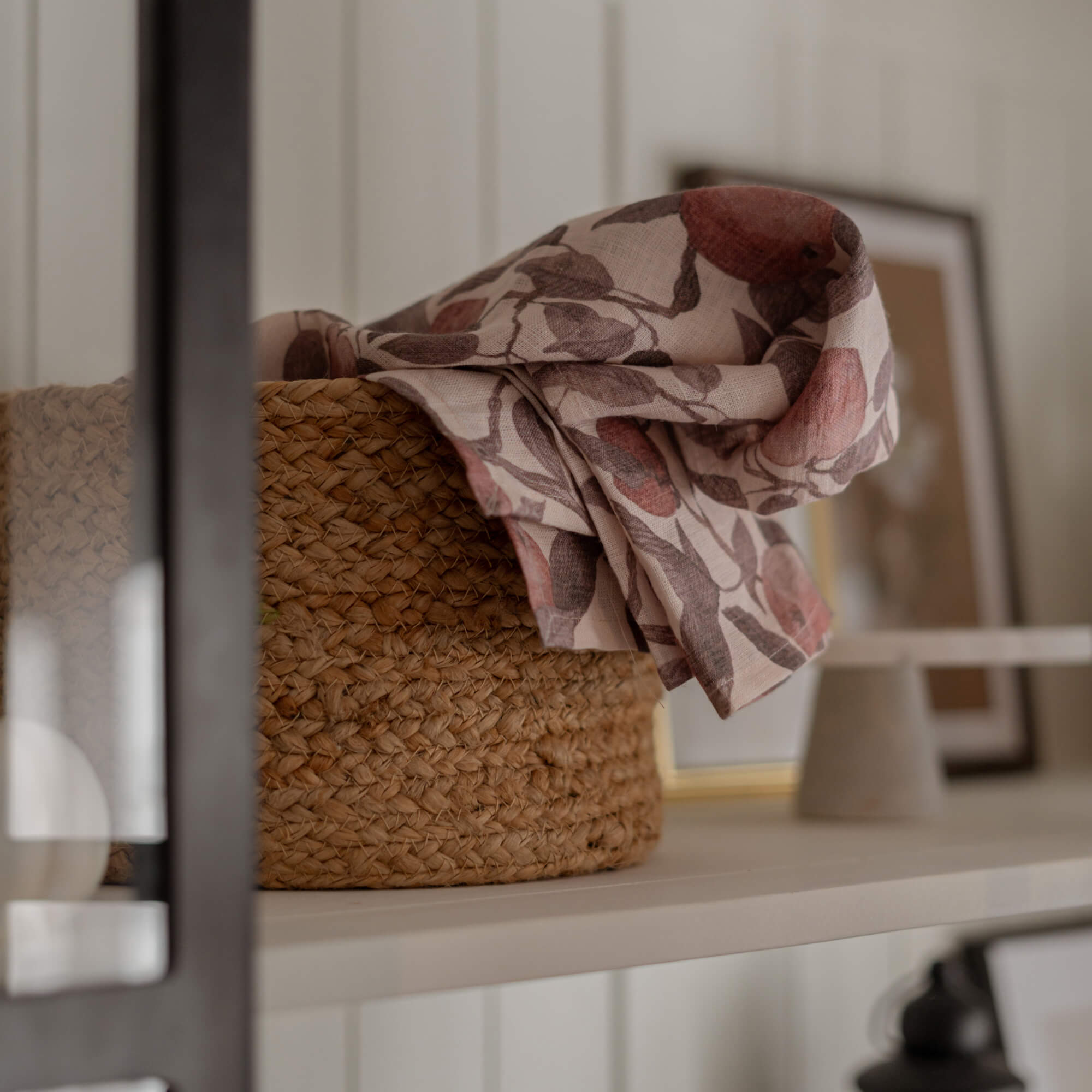 Geflochtener Naturkorb mit Leinenstoff in rosa-braunem Blumenmuster auf weißem Regal