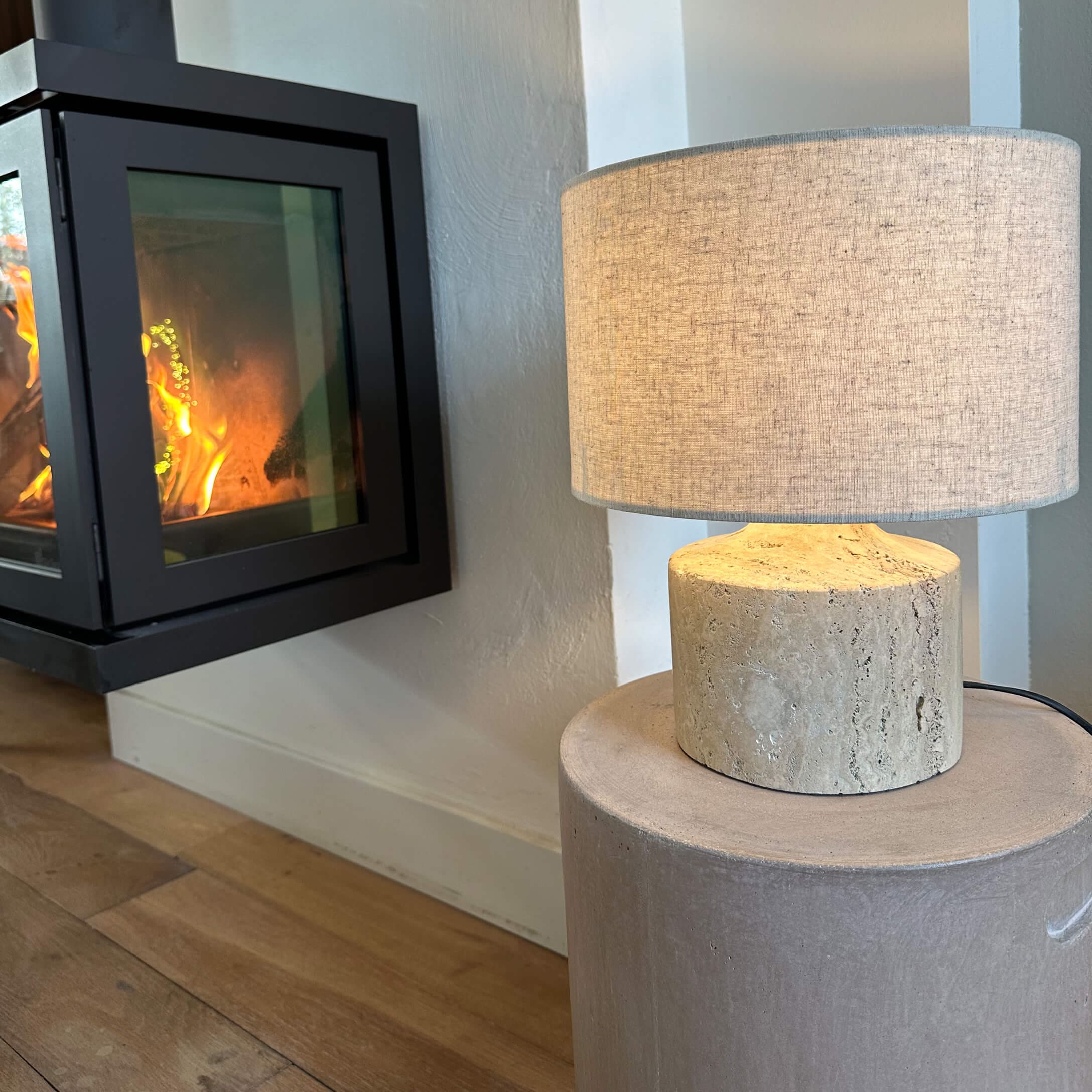 Tischlampe mit beigem Stoffschirm und heller Steinsockel neben brennendem Kamin