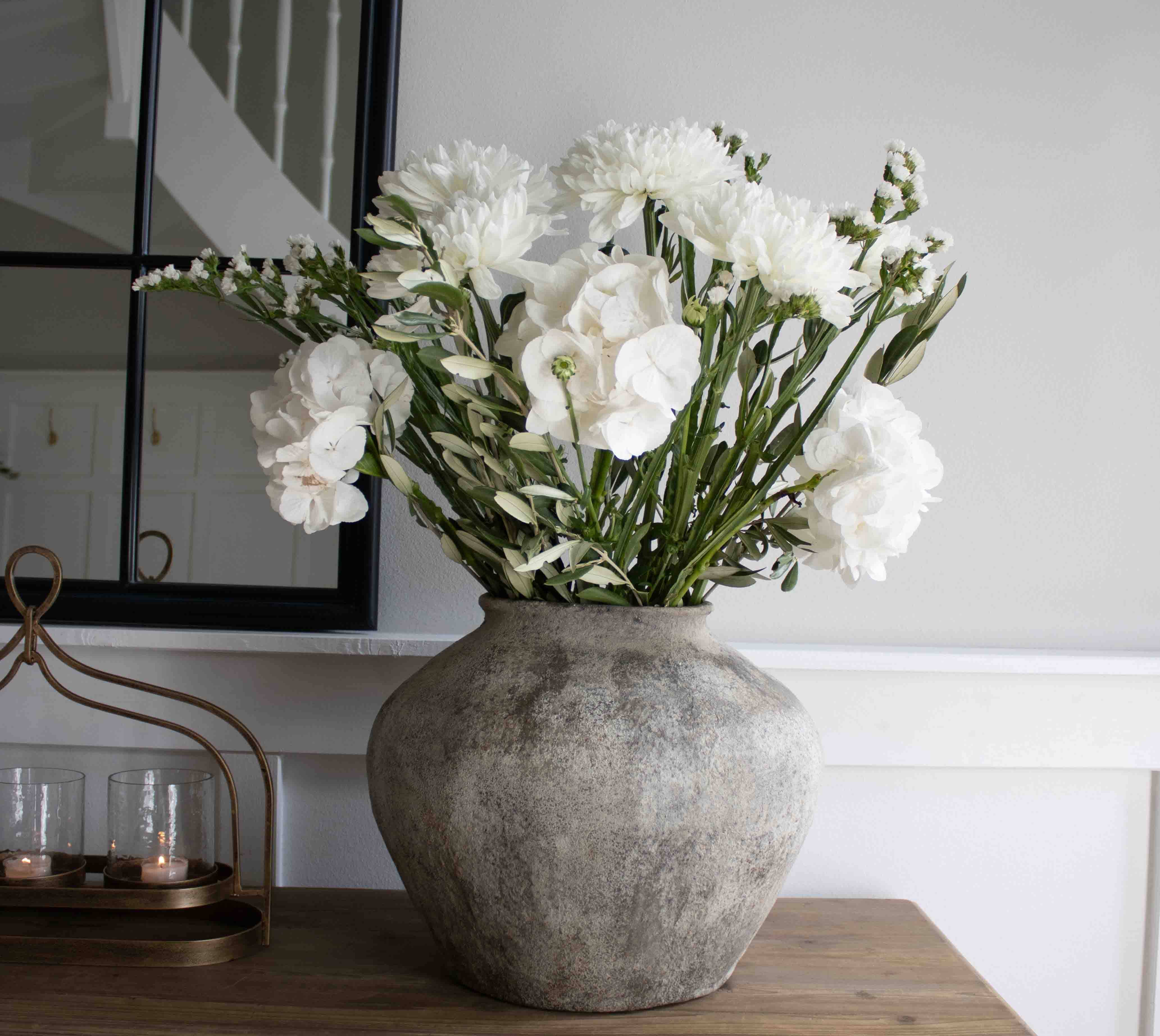 Große graue Steinvase mit weißen Dekoblumen auf einem Holztisch im Wohnzimmer