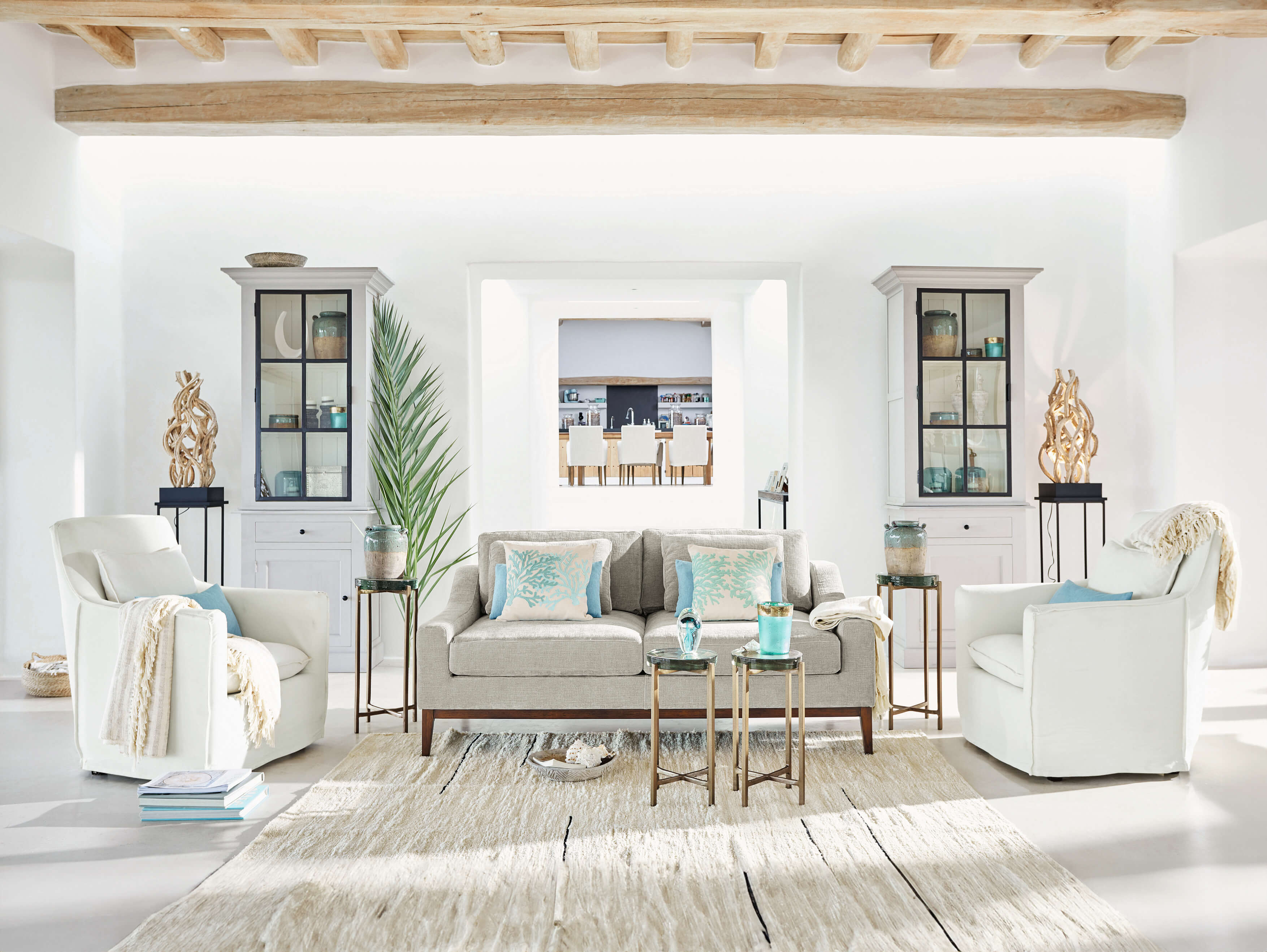 Helles Wohnzimmer mit grauem Sofa, weißen Sesseln und maritimen Dekorationen aus Naturholz