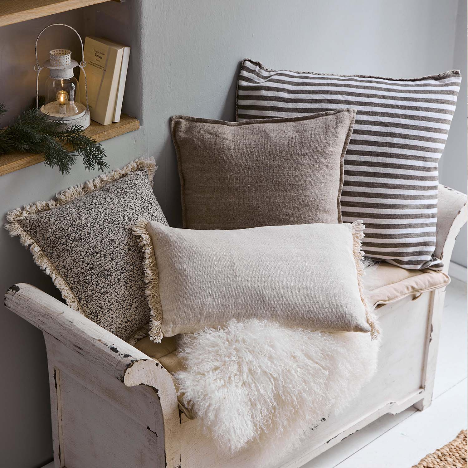 Set aus dekorativen Kissen in Beige- und Brauntönen auf weißer Holzbank mit flauschiger Decke