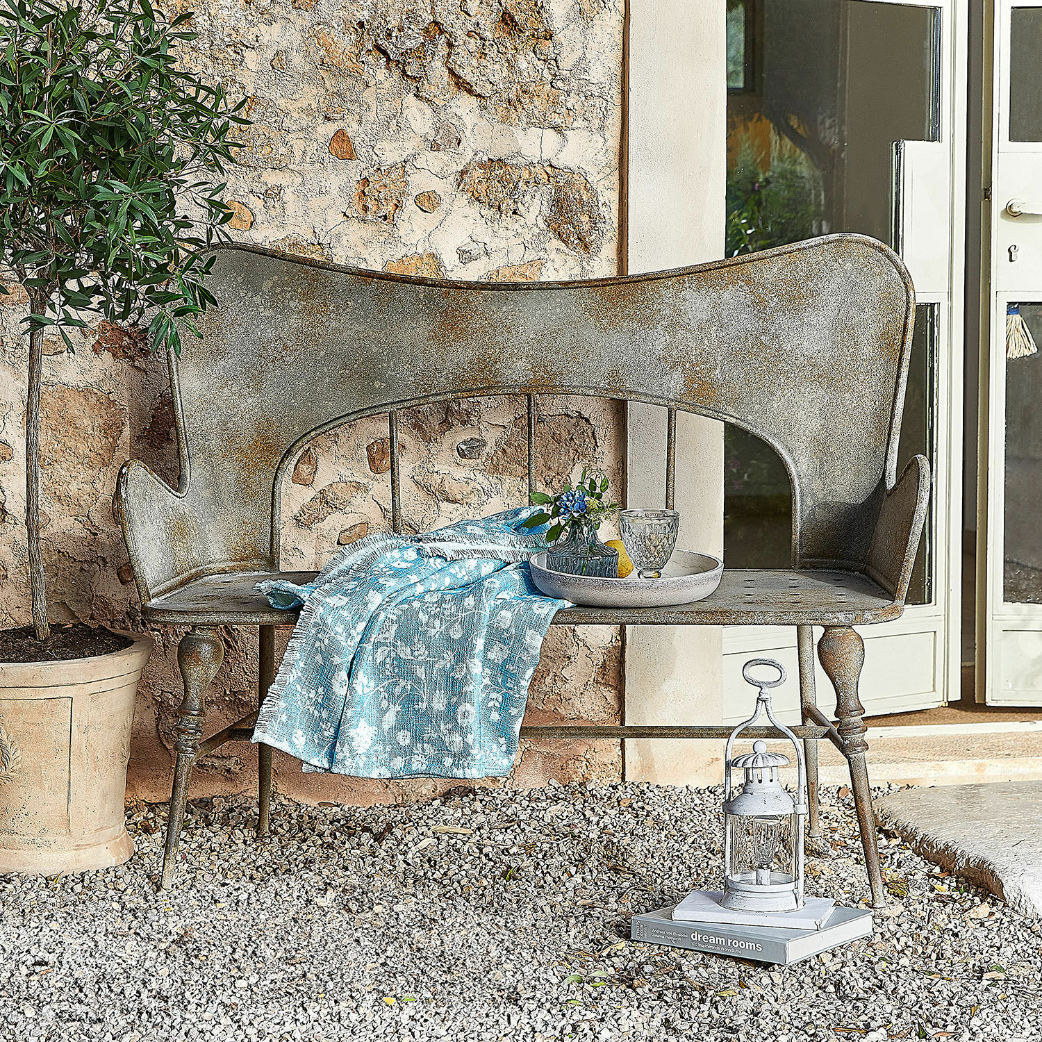 Bank Horivel Vintage Metallbank mit grauer Patina und blauem Tuch auf Kies vor Steinmauer im Garten