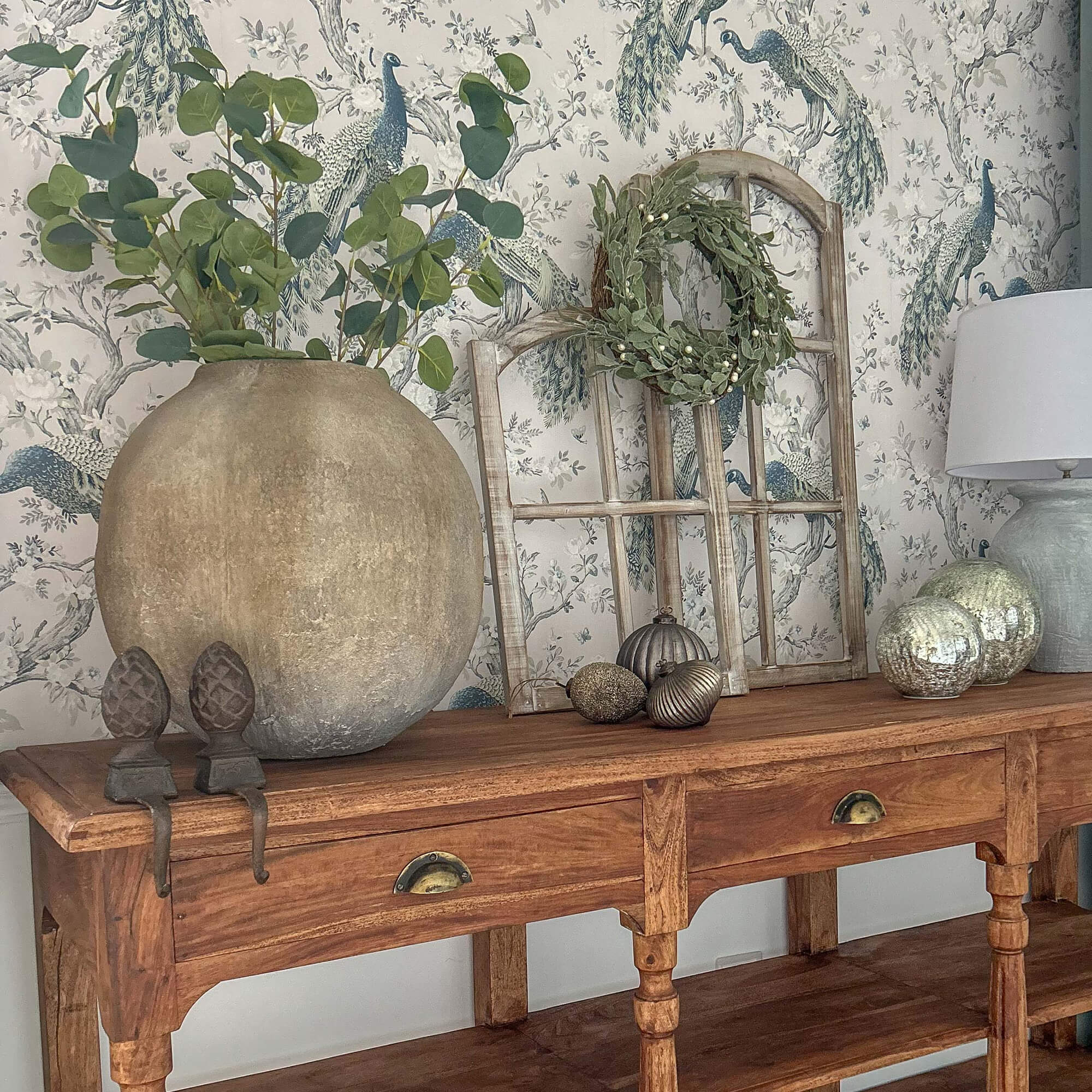 Holztisch mit großer Tonvase, grünen Blättern, Lampe und dekorativen Accessoires darauf