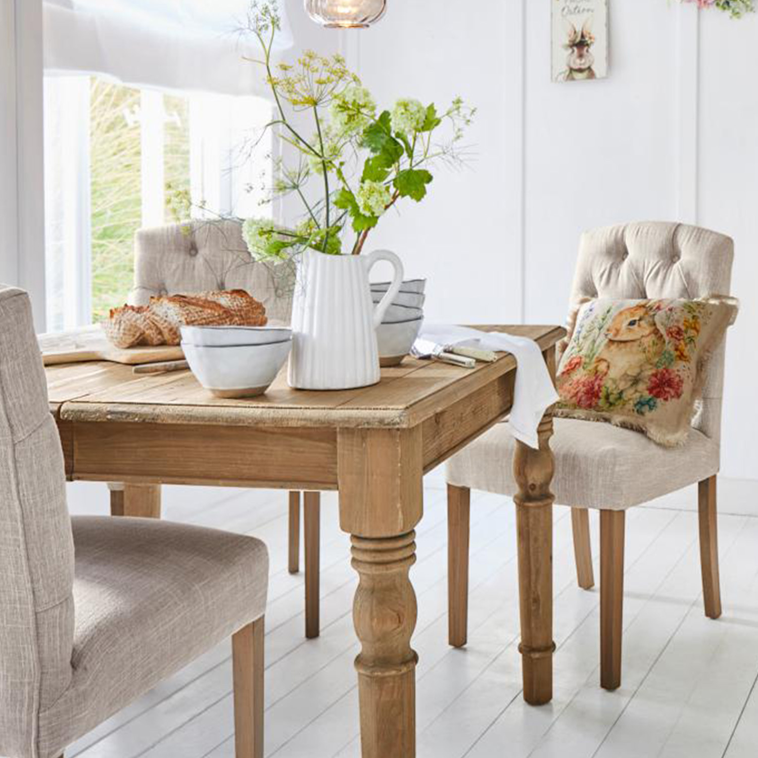 Heller Holztisch mit dekorativem Krug und Schalen, beige gepolsterte Stühle in einem hellen Esszimmer