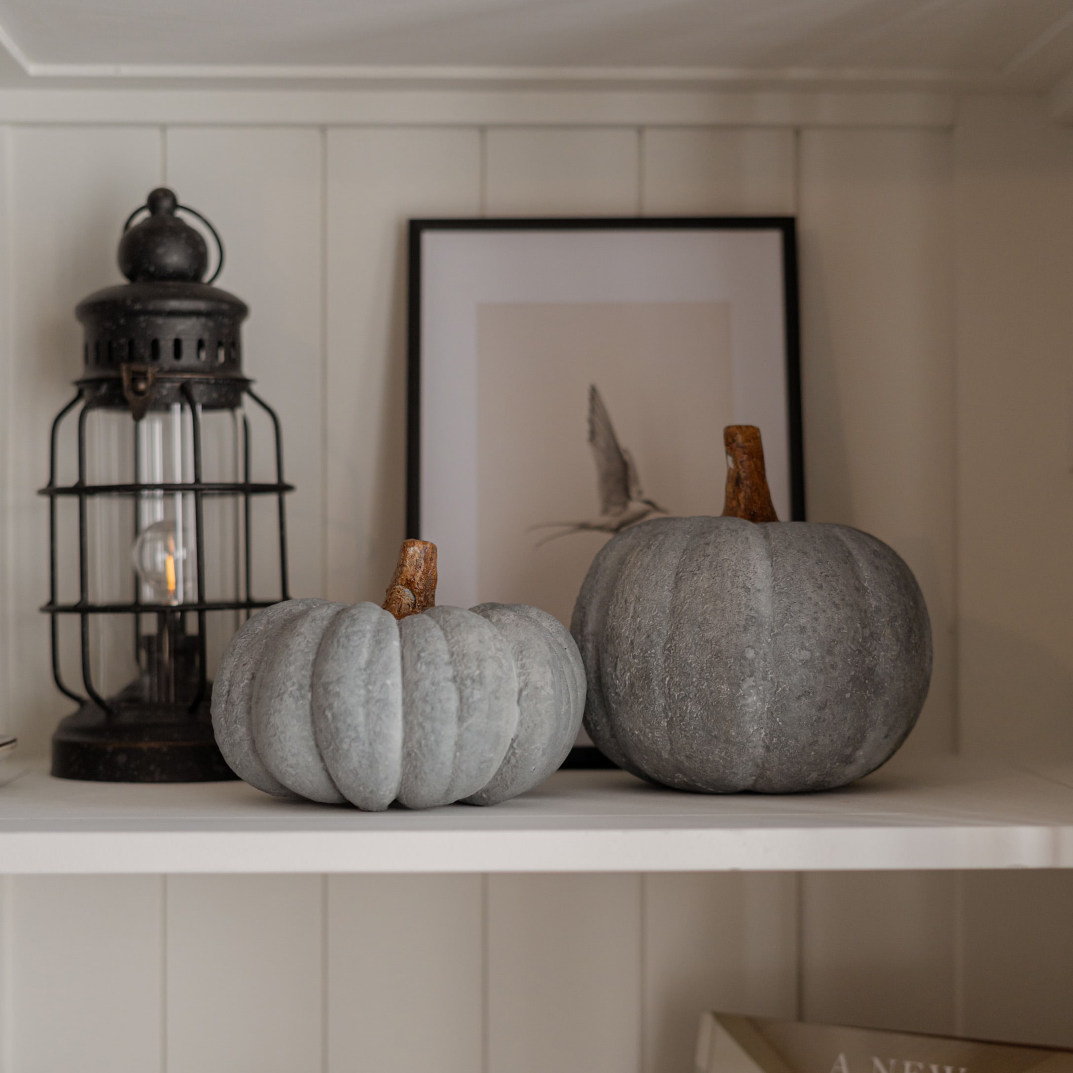 Zwei graue Deko-Kürbisse aus steinähnlichem Material auf weißem Regal im Landhausstil