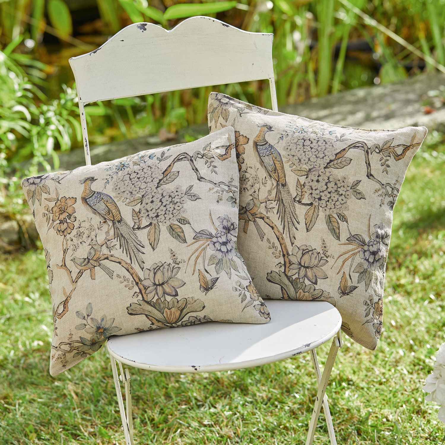 Kissenhülle 2er Set Lorry Zwei dekorative Baumwollkissen in Beige mit Vogel- und Blumenmuster auf weißem Stuhl im Garten