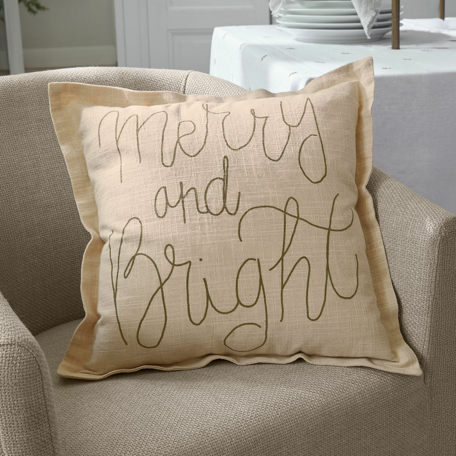 Kissenhülle Torvenna Beige Leinen-Dekokissen mit Schriftzug Merry and Bright auf beigem Sessel, Wohnaccessoire