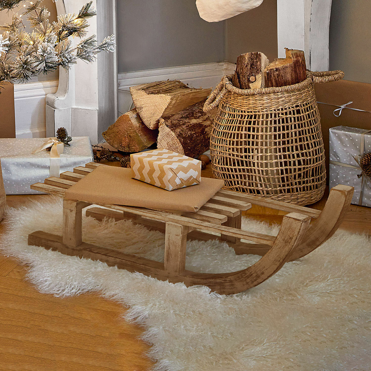 Deko-Schlitten FSC®-100% Hoekstra Dekorativer Holzschlitten auf weißem Fellteppich mit Geschenken und Korb mit Holzscheiten