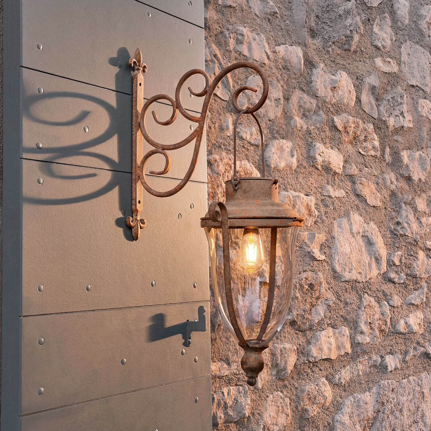Rustikale Außenwandleuchte aus Metall mit Rostoptik und klarem Glas an Steinmauer montiert