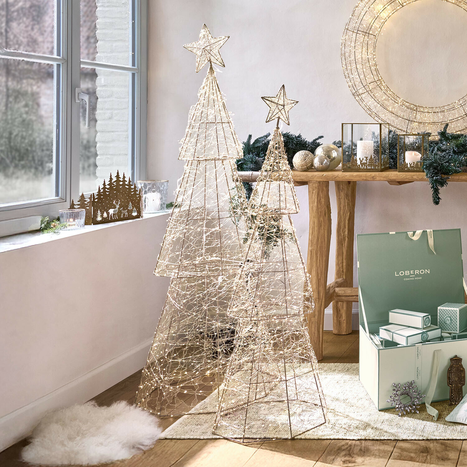 Zwei dekorative Weihnachtsbäume aus Metallgitter mit LED-Lichterketten in hellem Raum mit Weihnachtsdeko