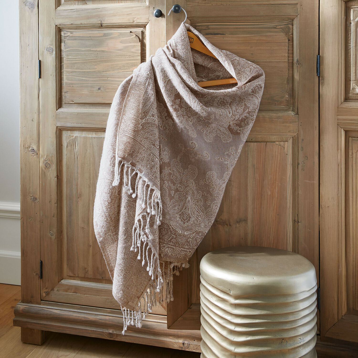 Beiger Schal mit Paisley-Muster und Fransen an einem Holzschrank, weiches Material, dekoratives Accessoire