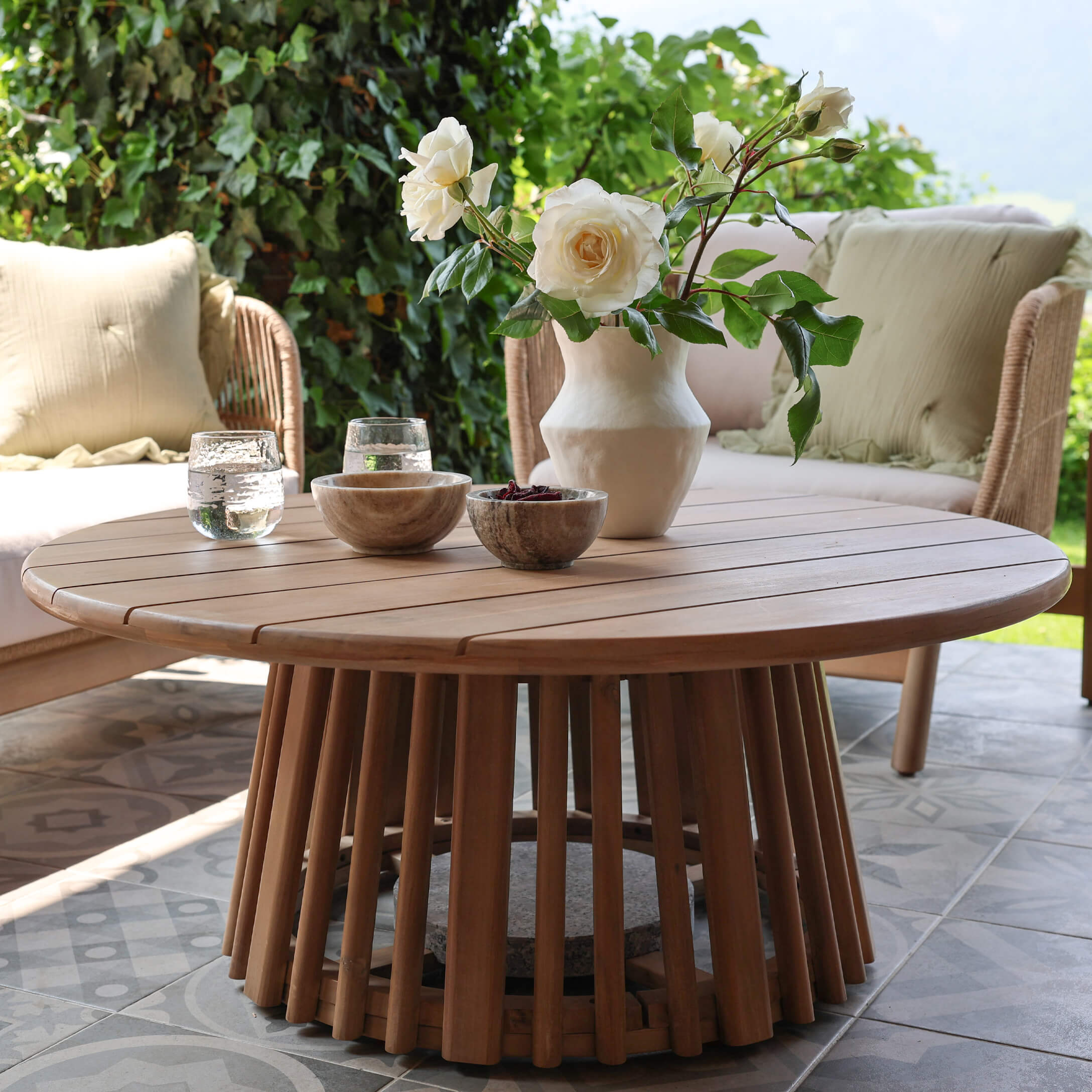 Runder Teakholz-Couchtisch in Naturfarbe auf Terrasse mit Blumendekor und Steinschalen