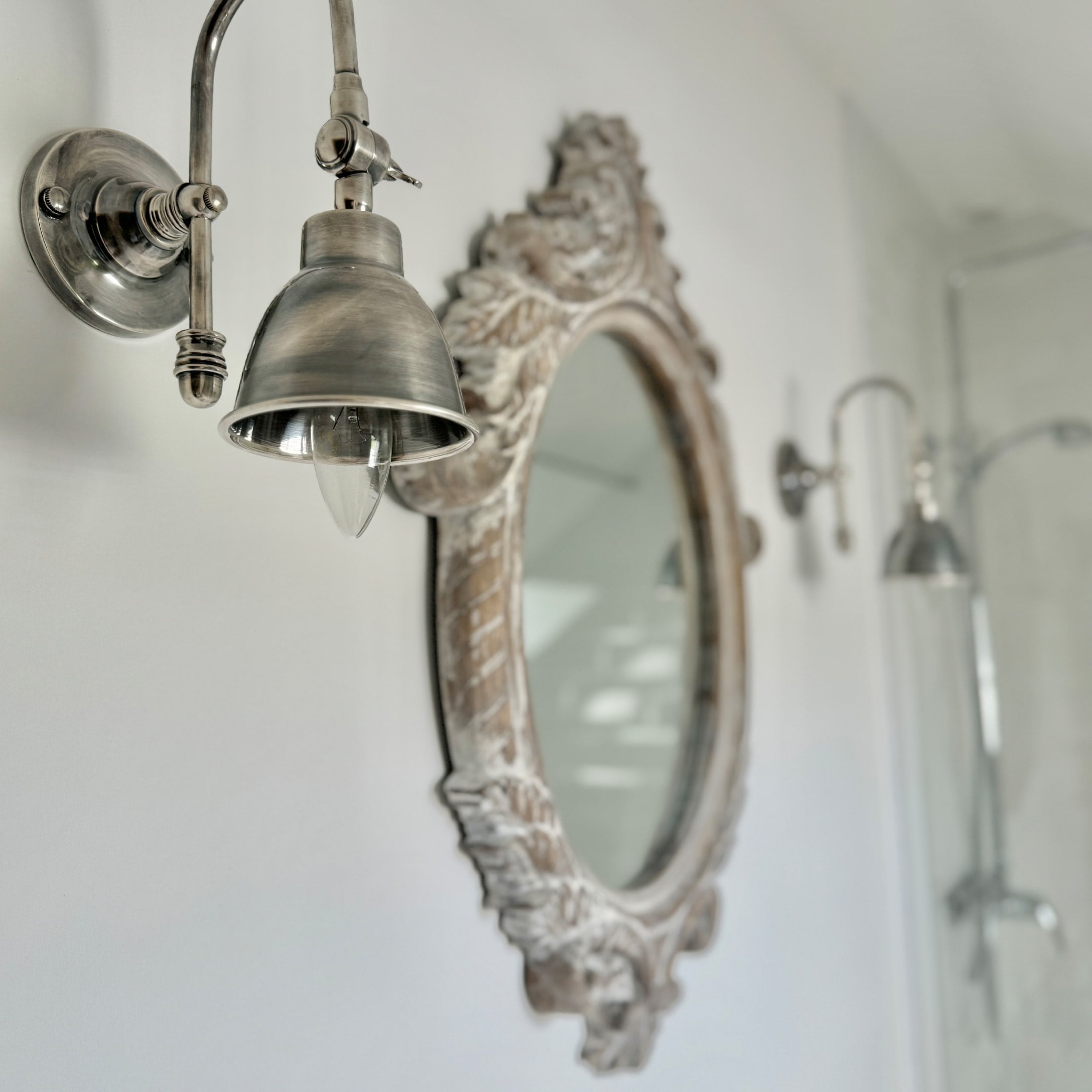 Vintage Metall-Wandleuchte im Badezimmer mit verziertem Holzrahmen-Spiegel an weißer Wand