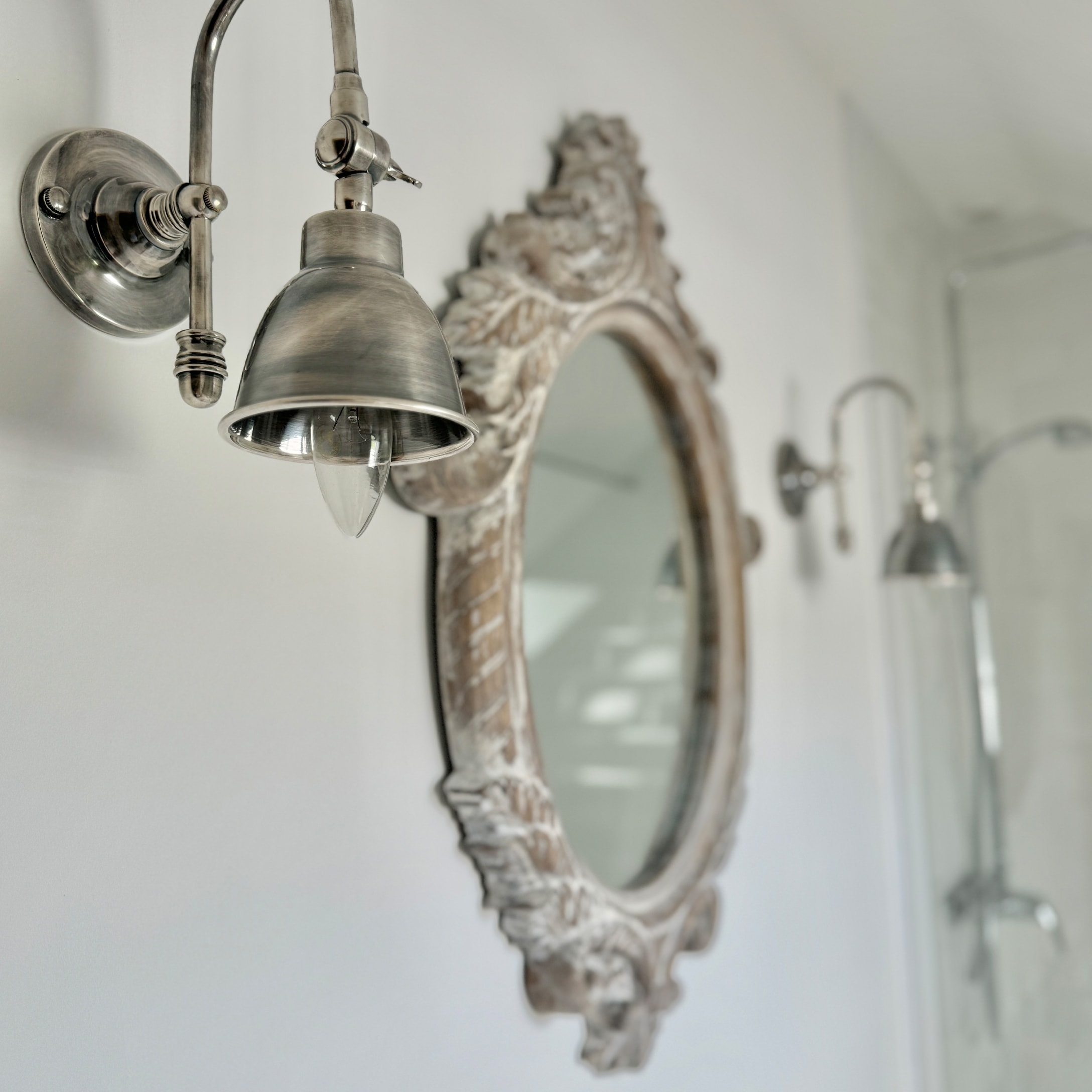 Vintage Metall-Wandleuchte im Badezimmer mit verziertem Holzrahmen-Spiegel an weißer Wand