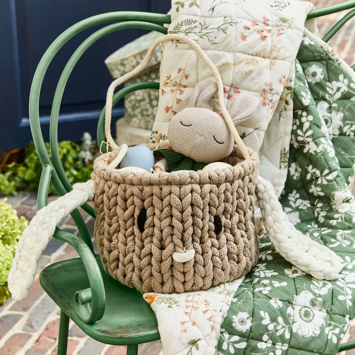 Brauner Korb aus geflochtenem Material mit Ohren und Hasenspielzeug, Osterdekoration auf grünem Stuhl