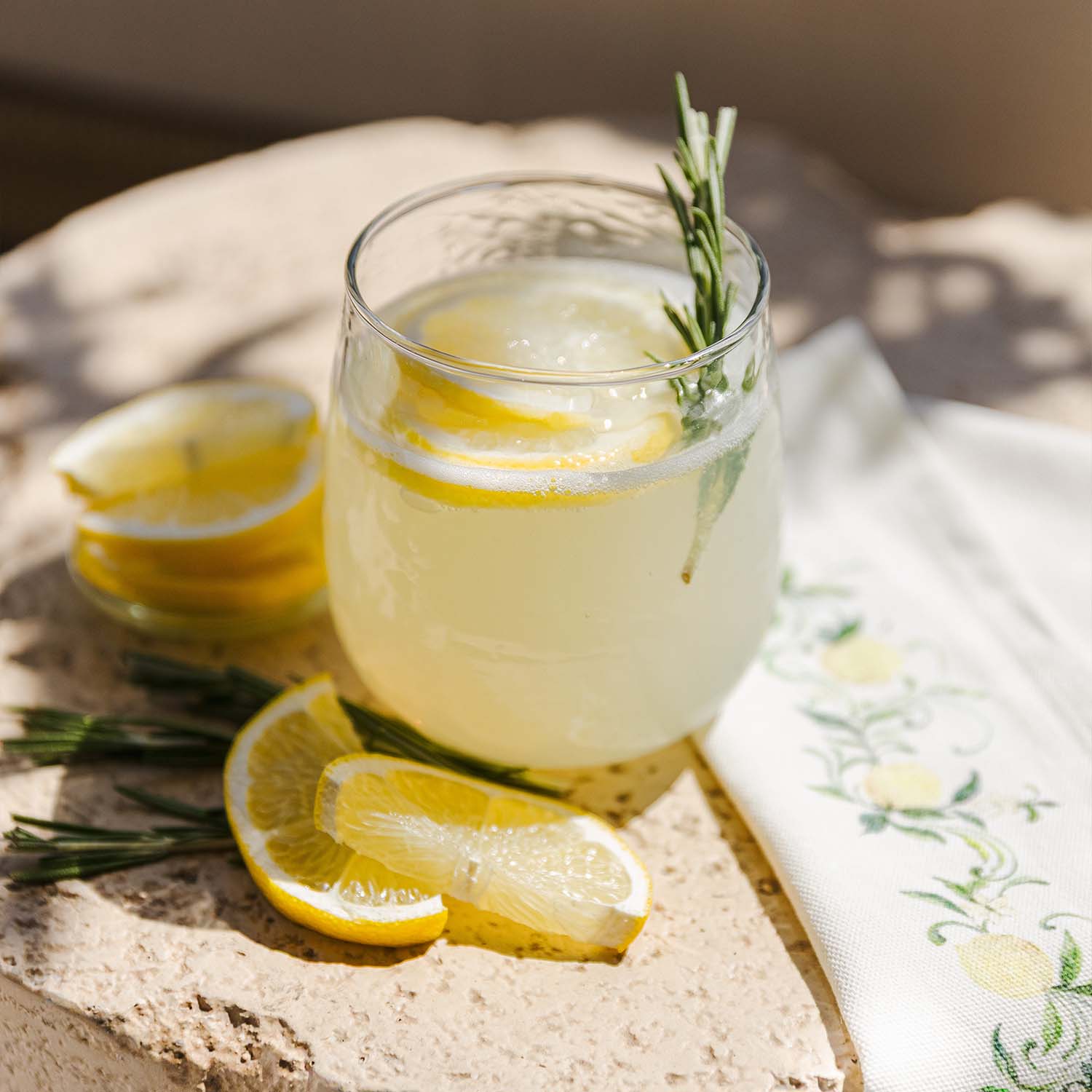 Glas Zitronenlimonade mit Zitronenscheiben und Rosmarinzweig auf Steinplatte mit Serviette
