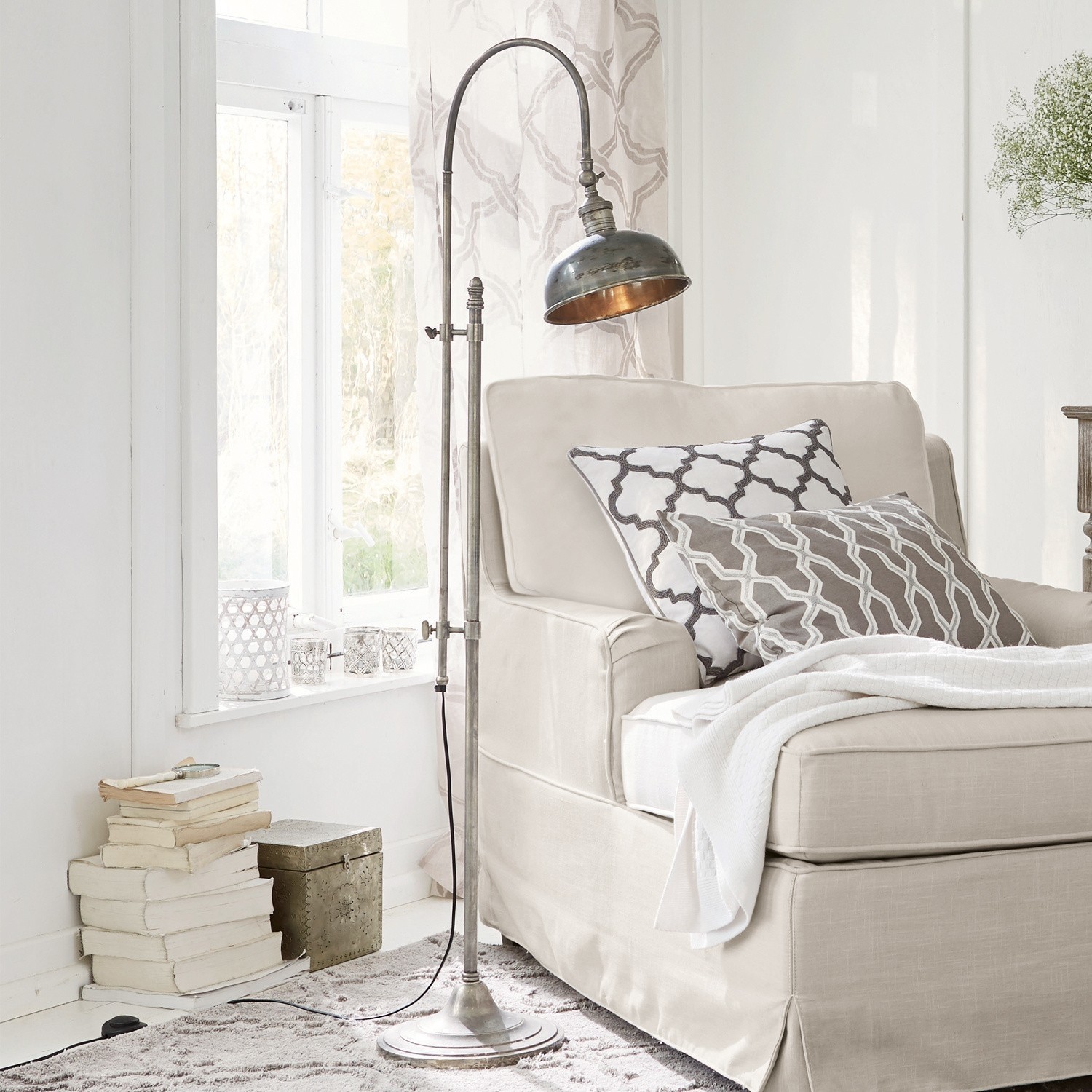 Metall Stehlampe im Vintage-Stil neben beigem Sofa mit Kissen und Decke im hellen Wohnzimmer