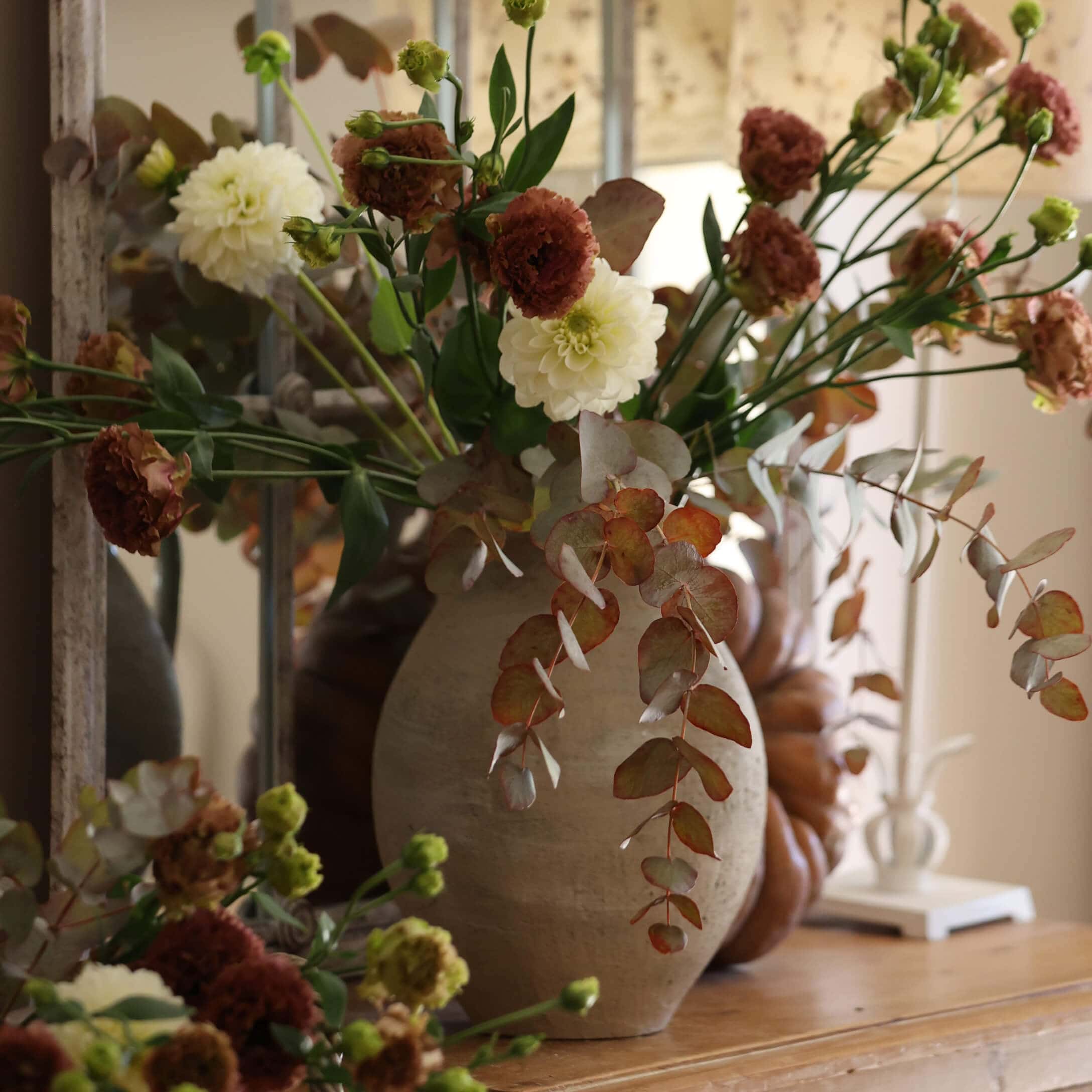 Beiger Keramikvase mit weiß-braunem Blumenstrauß auf dekorativem Holztisch