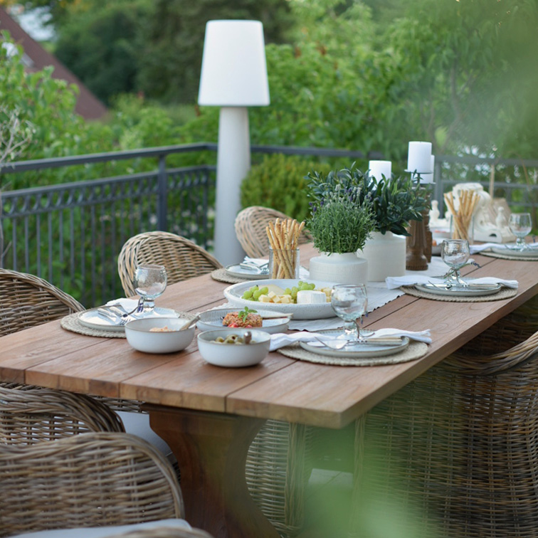 Holz-Gartentisch mit Rattanstühlen und Dekorationen für ein Sommeressen auf der Terrasse