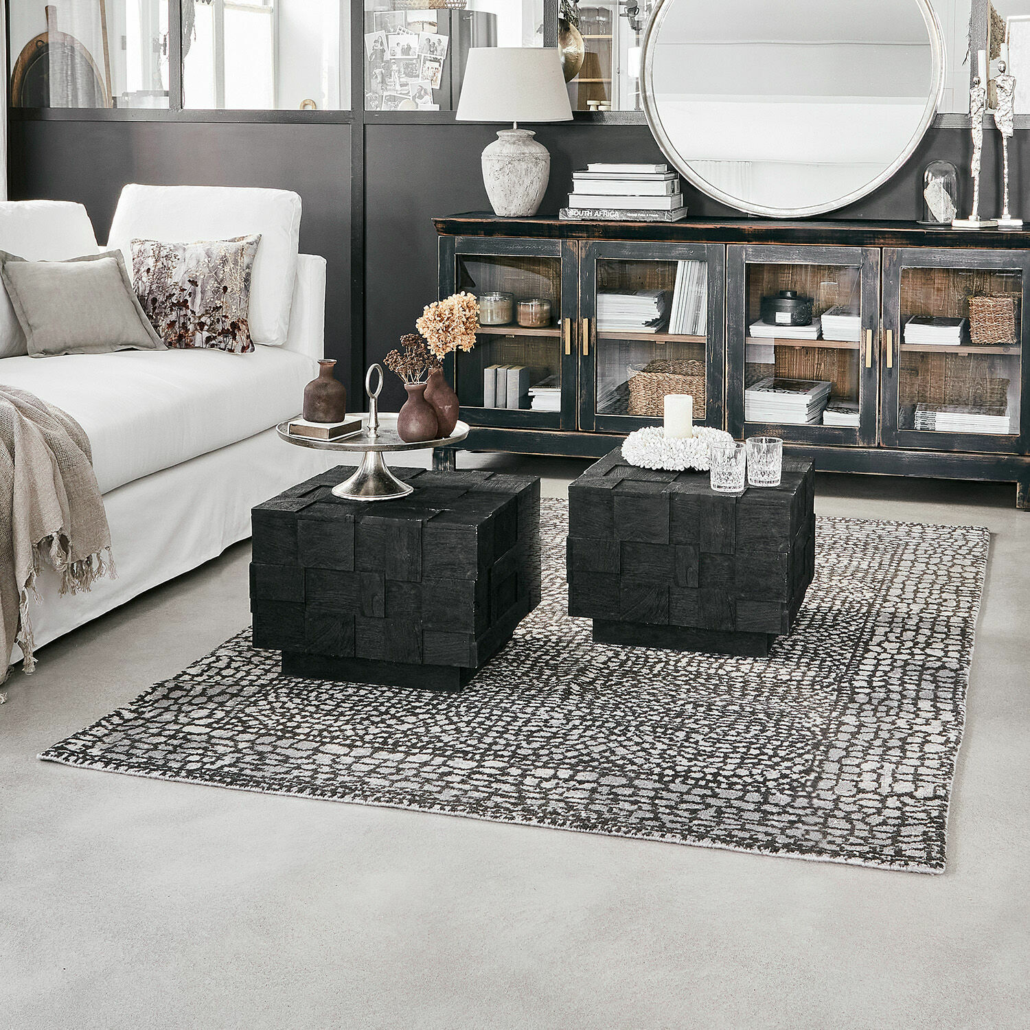 Modernes Wohnzimmer mit weißem Sofa und schwarzen Holzcouchtischen auf gemustertem Teppich