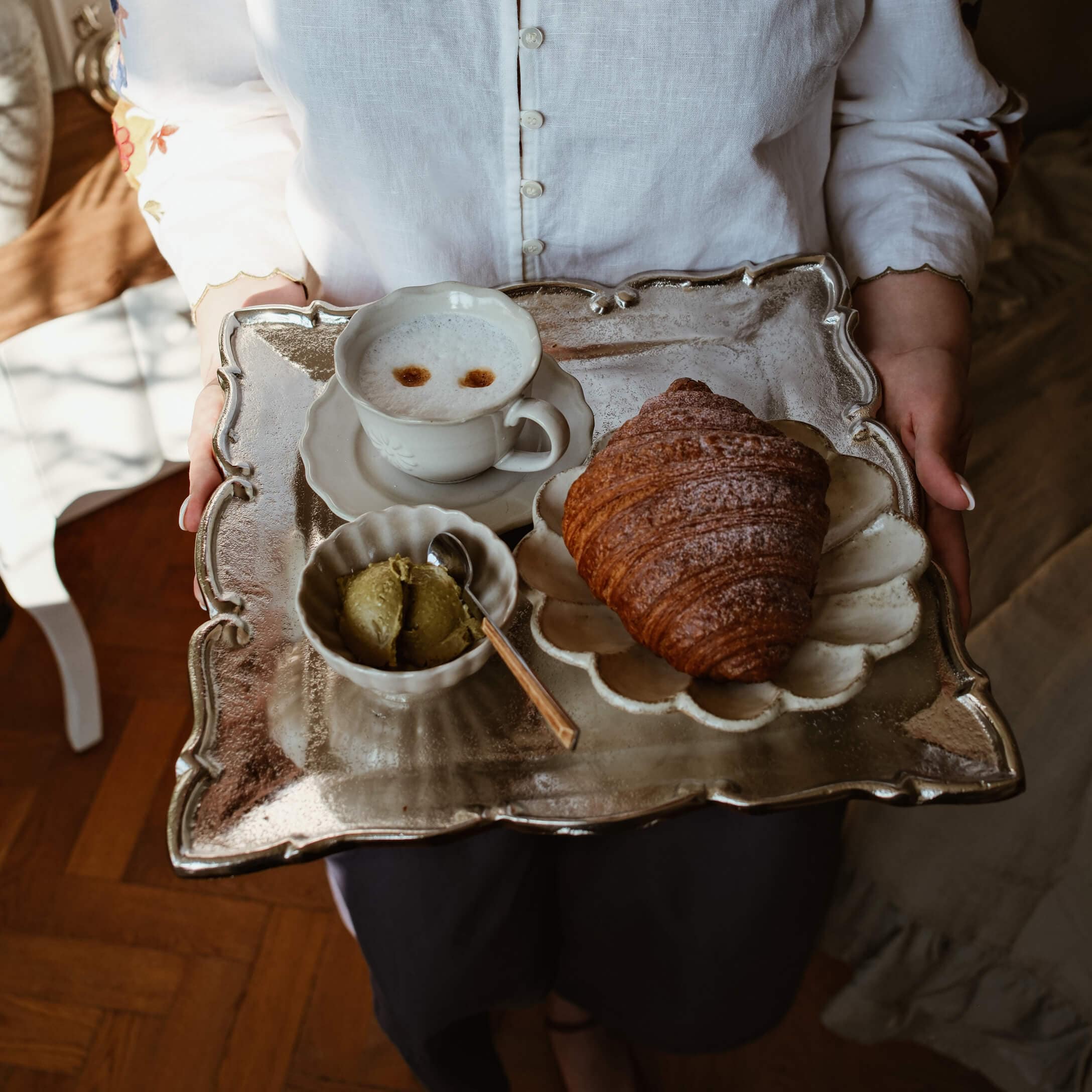 Metalltablett mit Croissant, Kaffeetasse und grünem Butteraufstrich auf weißem Porzellan