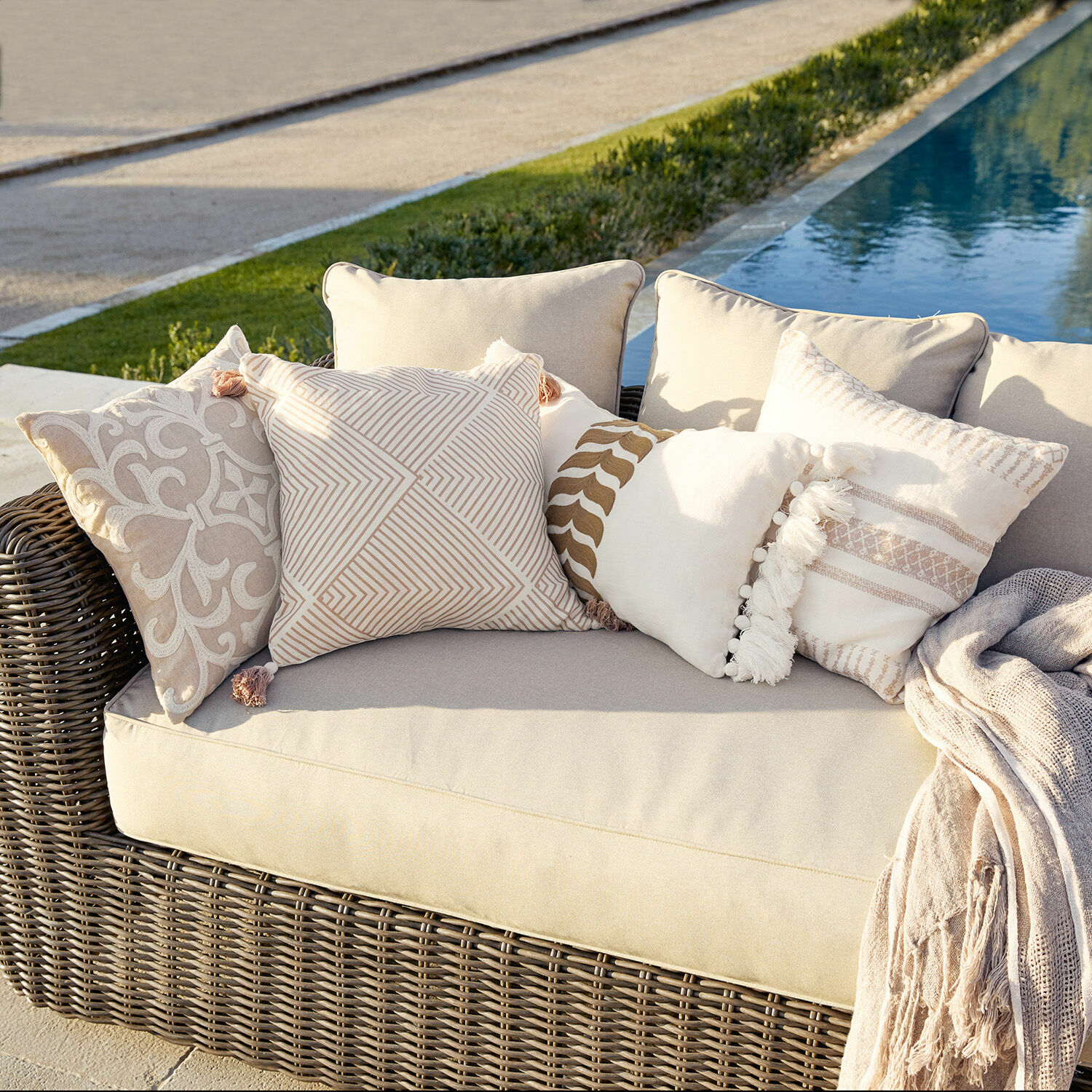 Kissenhülle 4er Set Olette Beiges Rattan-Sofa mit cremefarbenen und beigen Dekokissen draußen am Pool