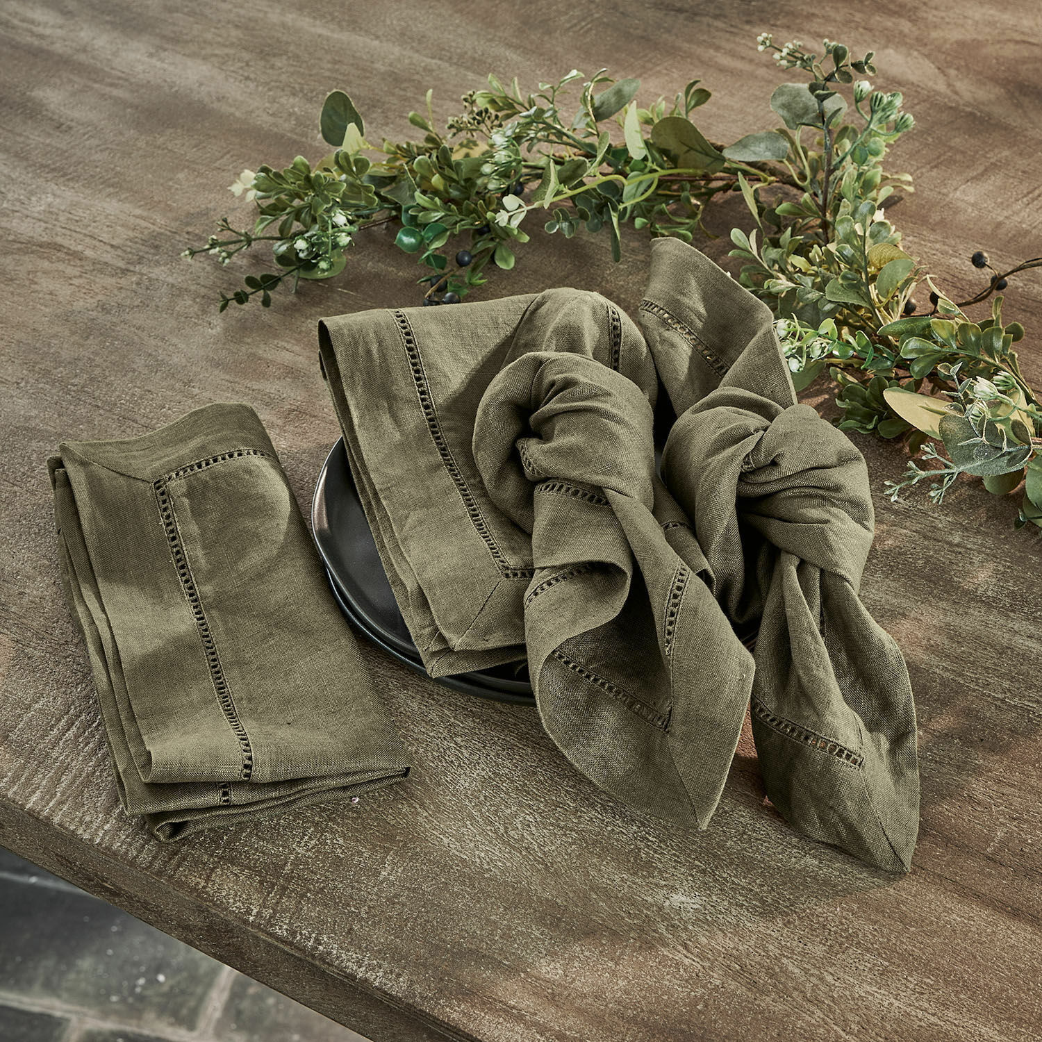 Serviette 4er Set Covent Garden Set aus grünen Leinenservietten mit dekorativer Naht auf Holztisch mit Pflanzenarrangement