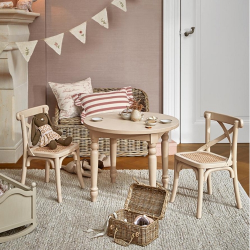 Runder Holztisch mit zwei Stühlen und einem Weidenkorb auf Teppich in hellem Kinderzimmer