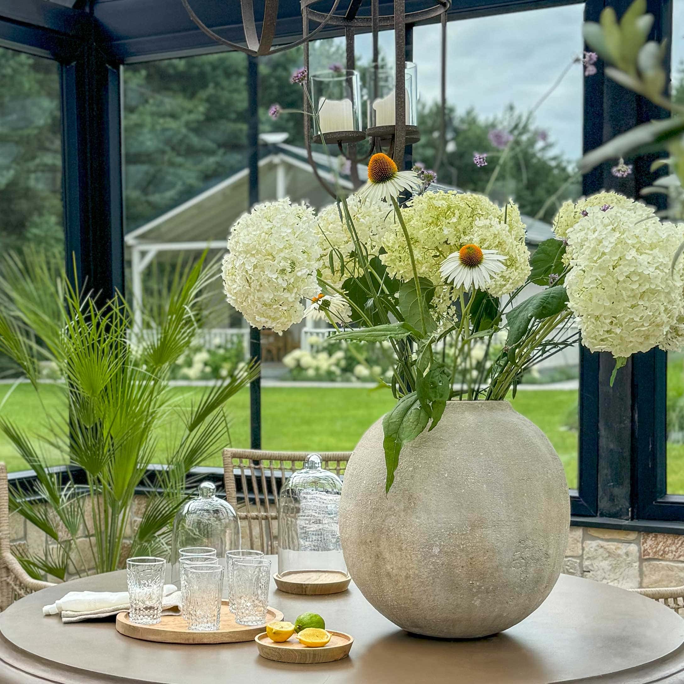 Große runde Betonvase mit weißen Blumen auf Gartentisch, Wohn- und Gartenmöbel Dekoration