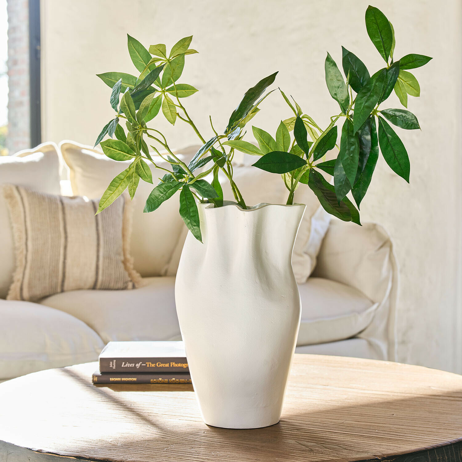 Weiße Keramikvase mit wellenförmiger Form und grünen Blättern auf Holztisch im Wohnzimmer