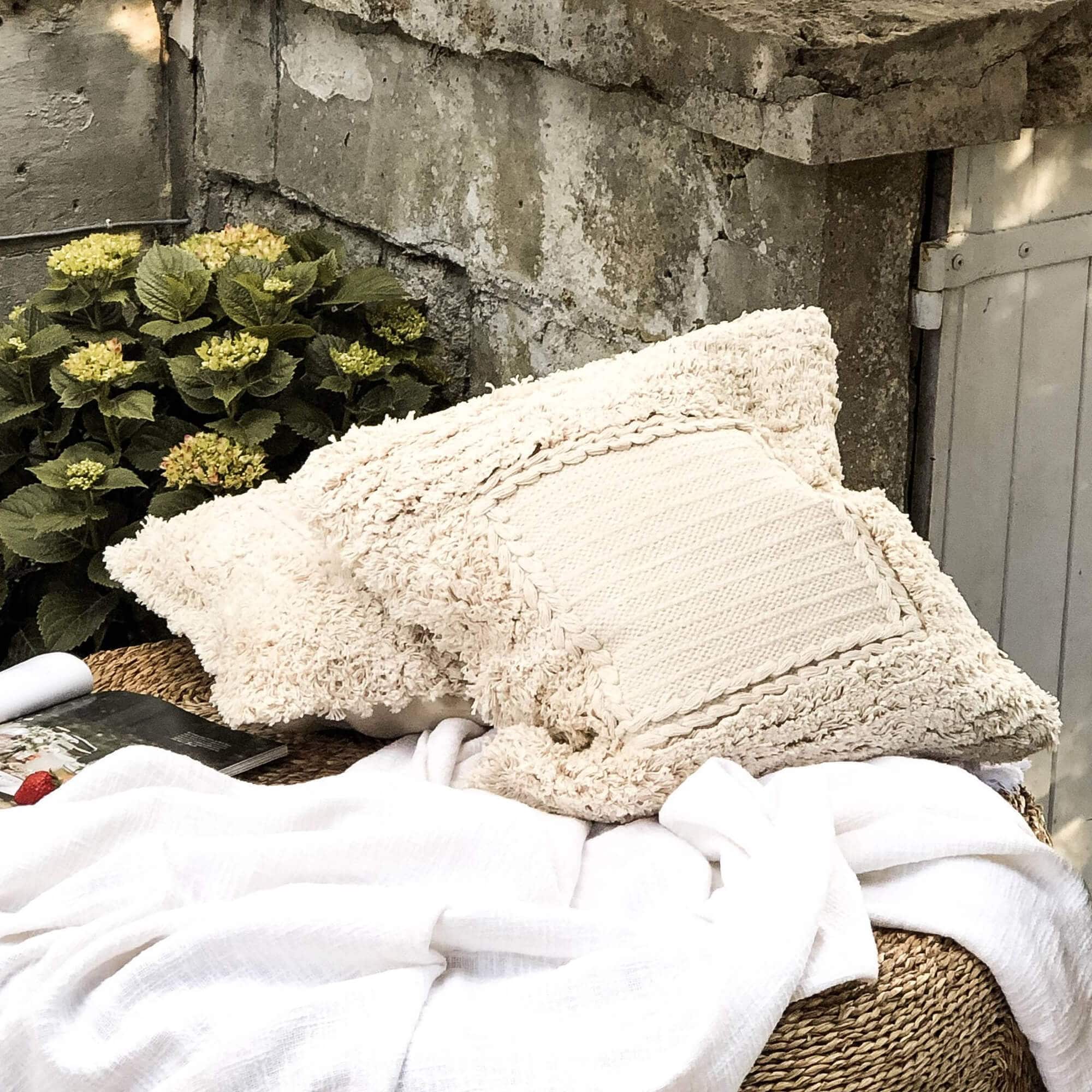 Beige Dekokissen aus weichem Material auf geflochtenem Gartenmöbel mit weißer Decke